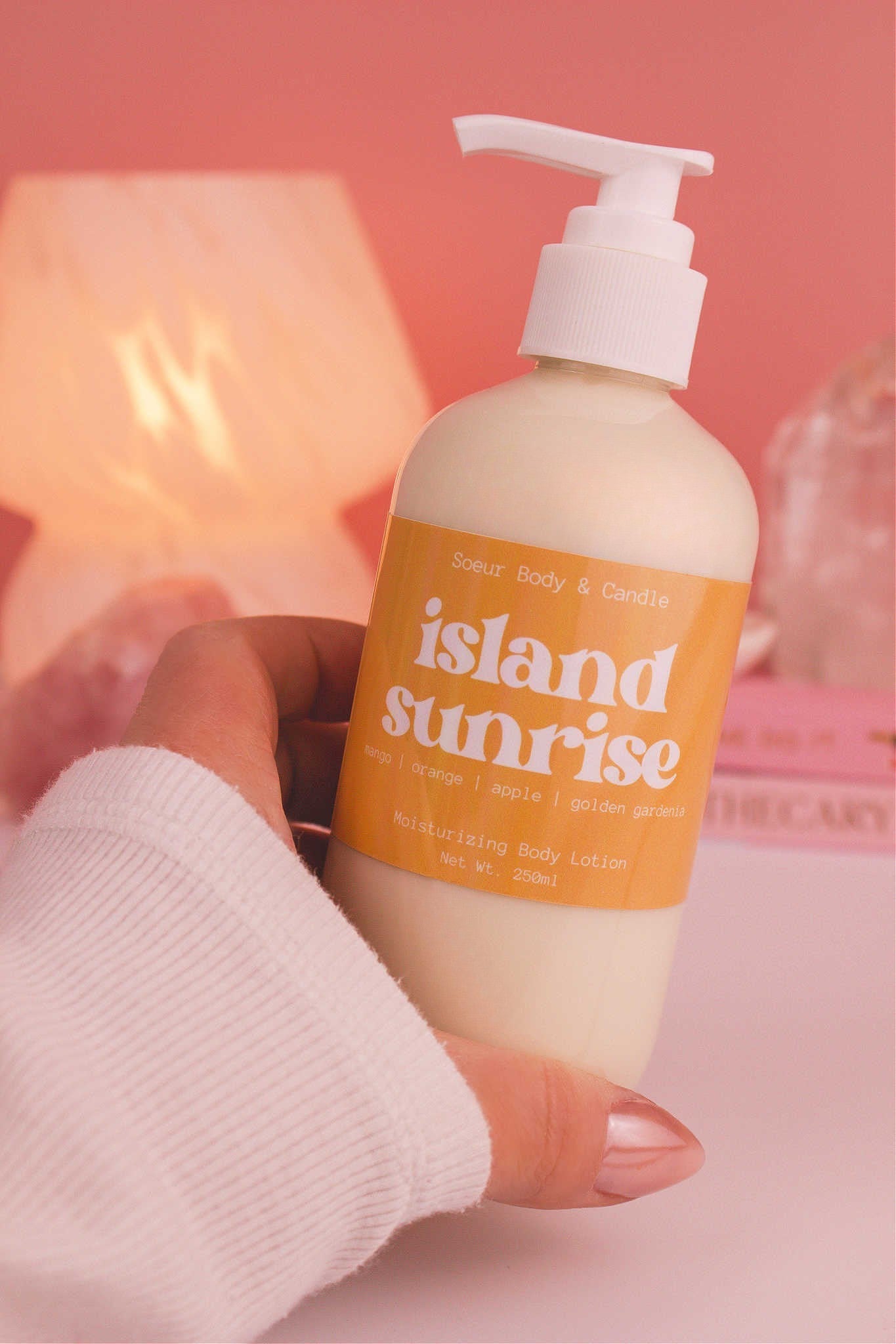 Close-up of a hand holding the Island Sunrise body lotion, highlighting its smooth texture and refreshing scent of mango, orange, apple, and golden gardenia.