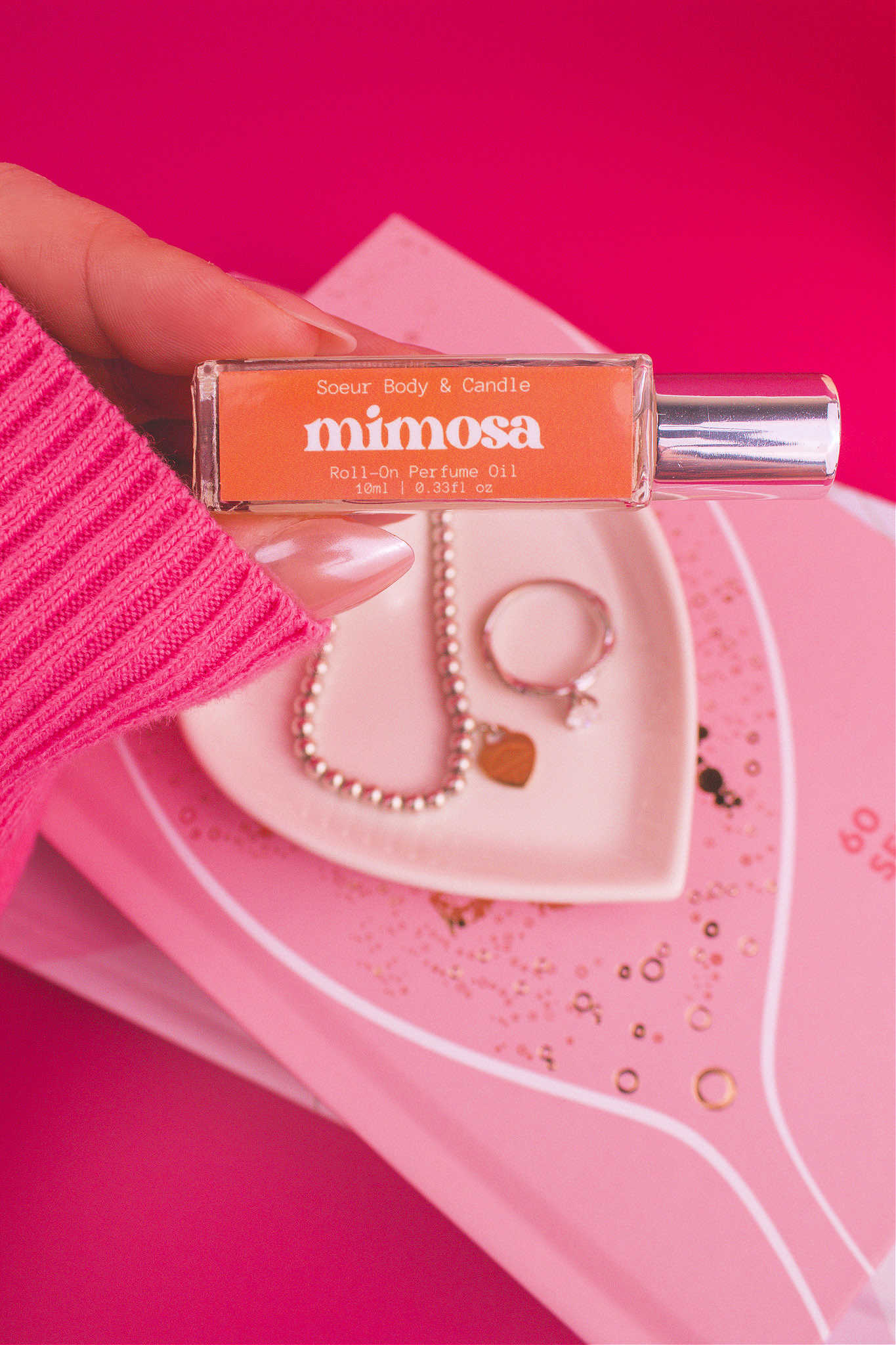 Close-up shot of Mimosa roll-on perfume held in hand with a jewelry dish and jewelry in the background, capturing its fruity mix of orange, neroli, honeysuckle, and vanilla.