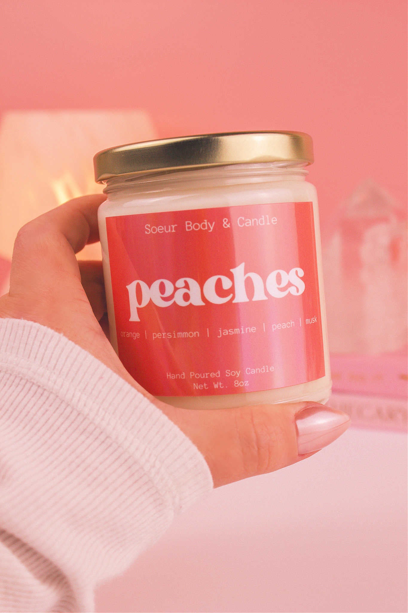Close-up of a hand holding the Peaches candle, showcasing its design and fragrance notes of orange, persimmon, jasmine, peach, and musk.