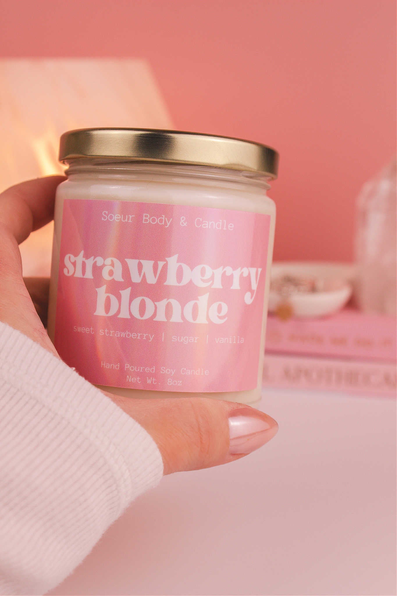 Close-up of a hand holding the Strawberry Blonde candle, showcasing its design and fragrance notes of sweet strawberry, sugar, and vanilla.