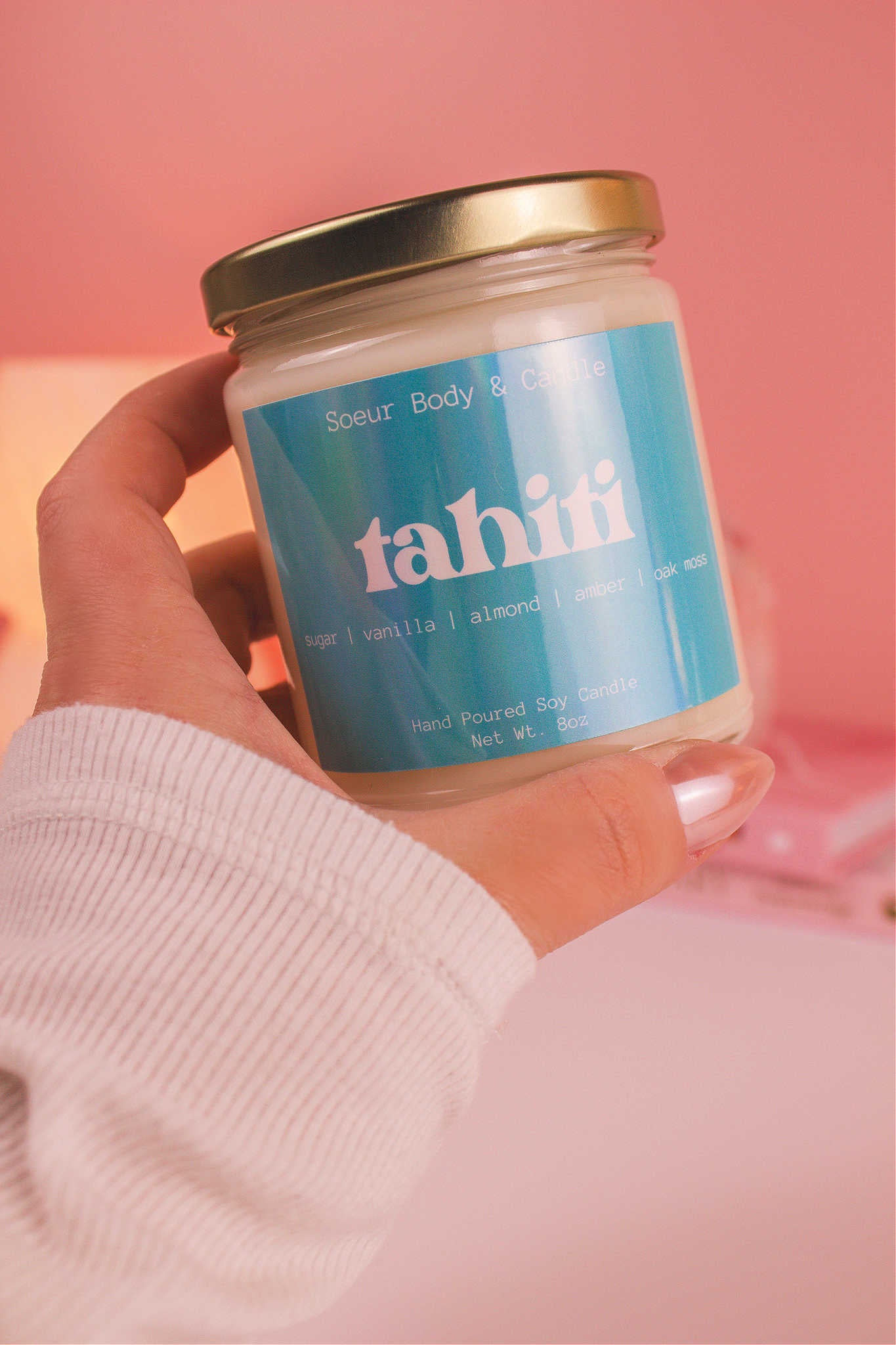 Close-up of a hand holding the Tahiti candle, showcasing its design and fragrance notes of sugar, vanilla, almond, amber, and oak moss.
