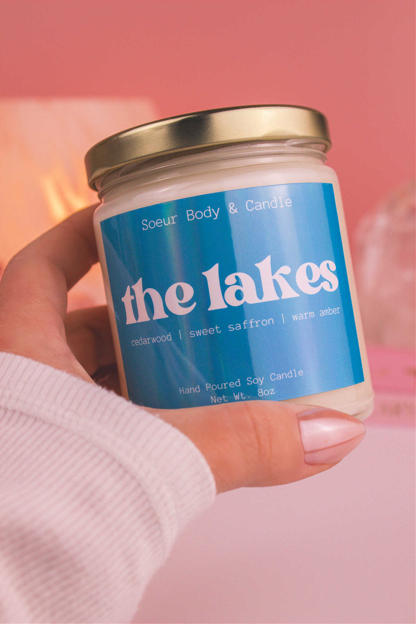 Close-up of a hand holding The Lakes candle, showcasing its design and fragrance notes of cedarwood, sweet saffron, and warm amber.