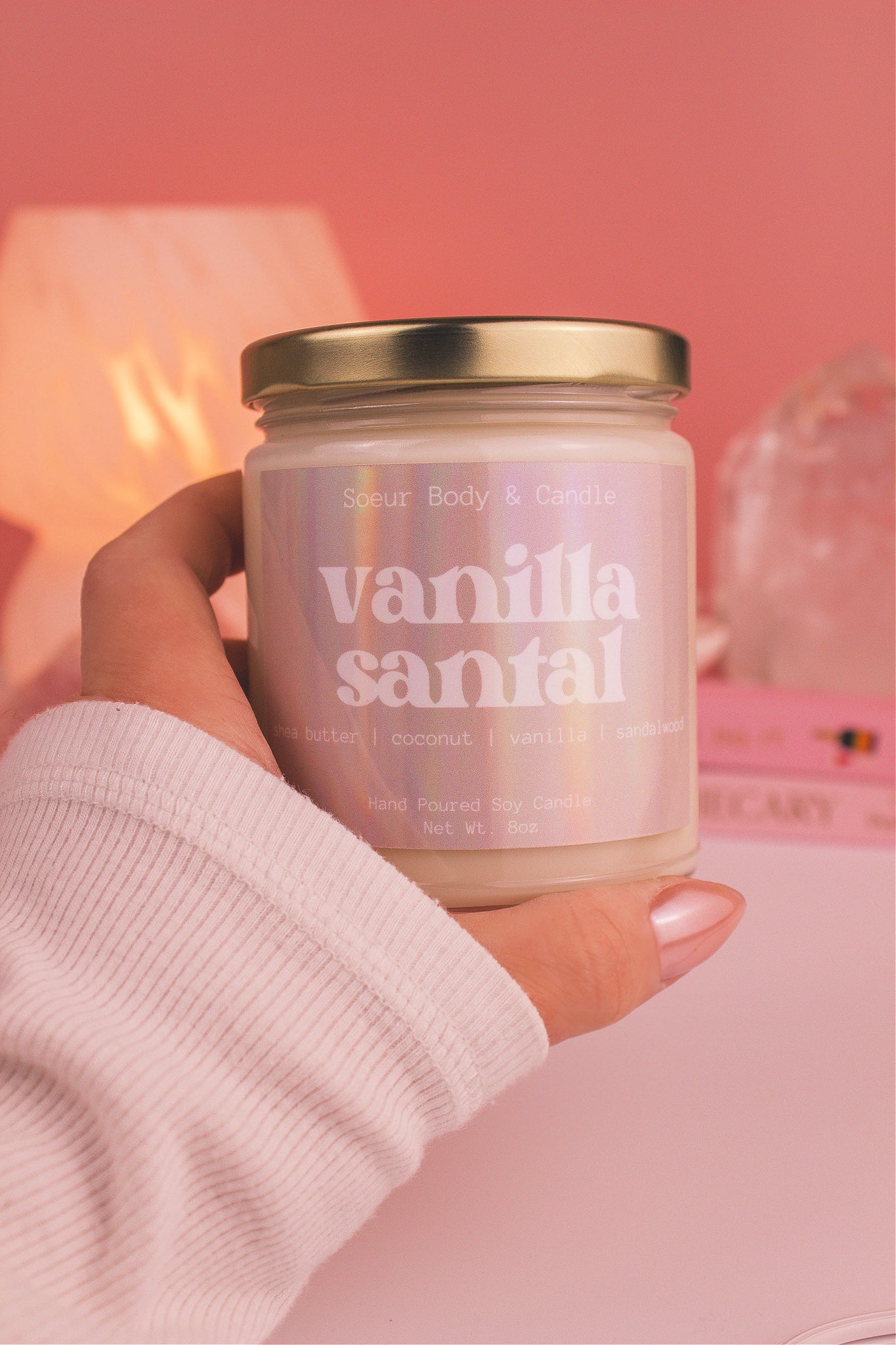 Close-up of a hand holding the Vanilla Santal candle, showcasing its design and fragrance notes of shea butter, coconut, vanilla, and sandalwood.