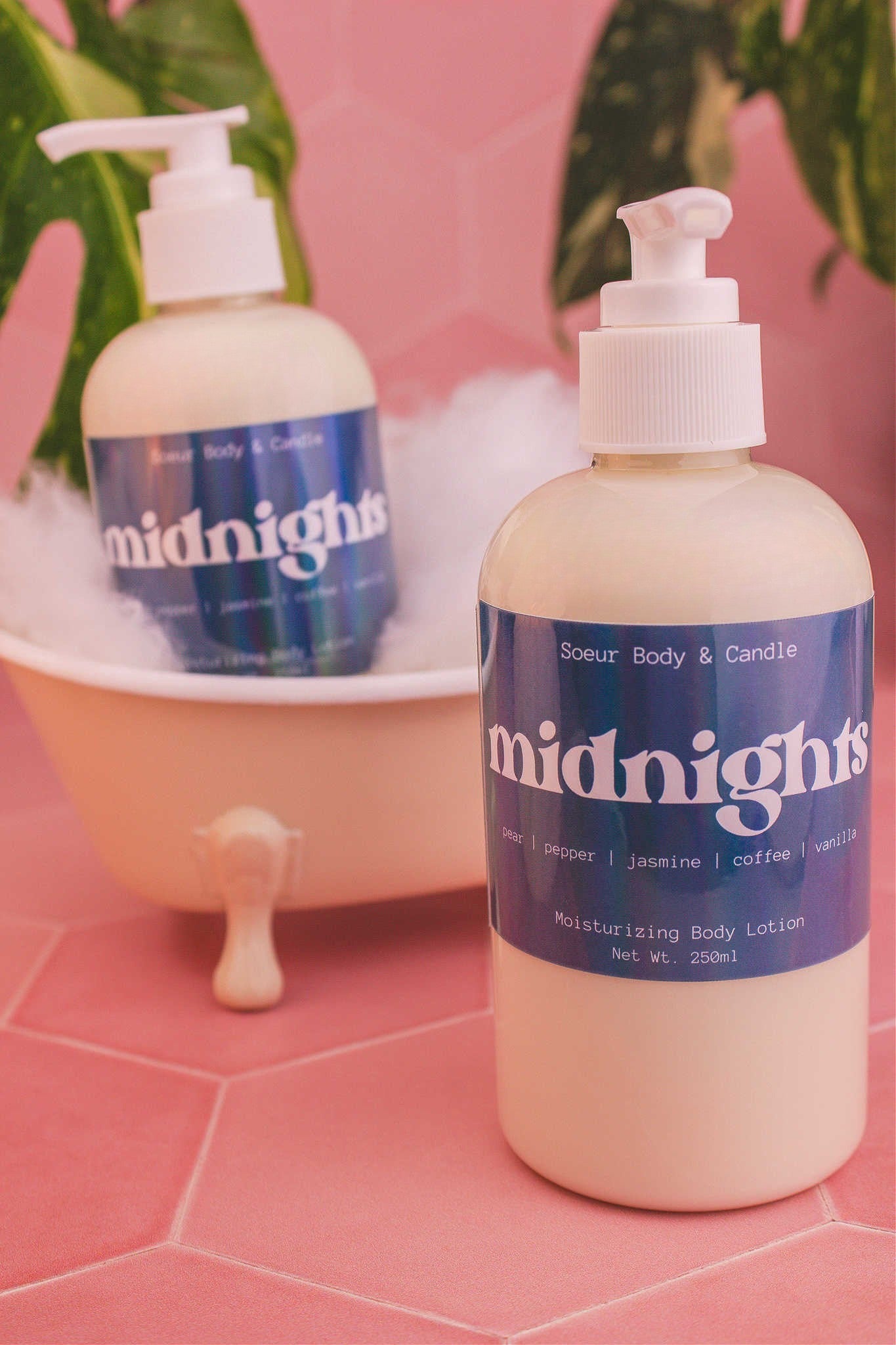 Display of two Midnights body lotions in a small tub with bubbles and plants in the background, evoking a relaxing vibe with pear, pepper, jasmine, coffee, and vanilla notes.