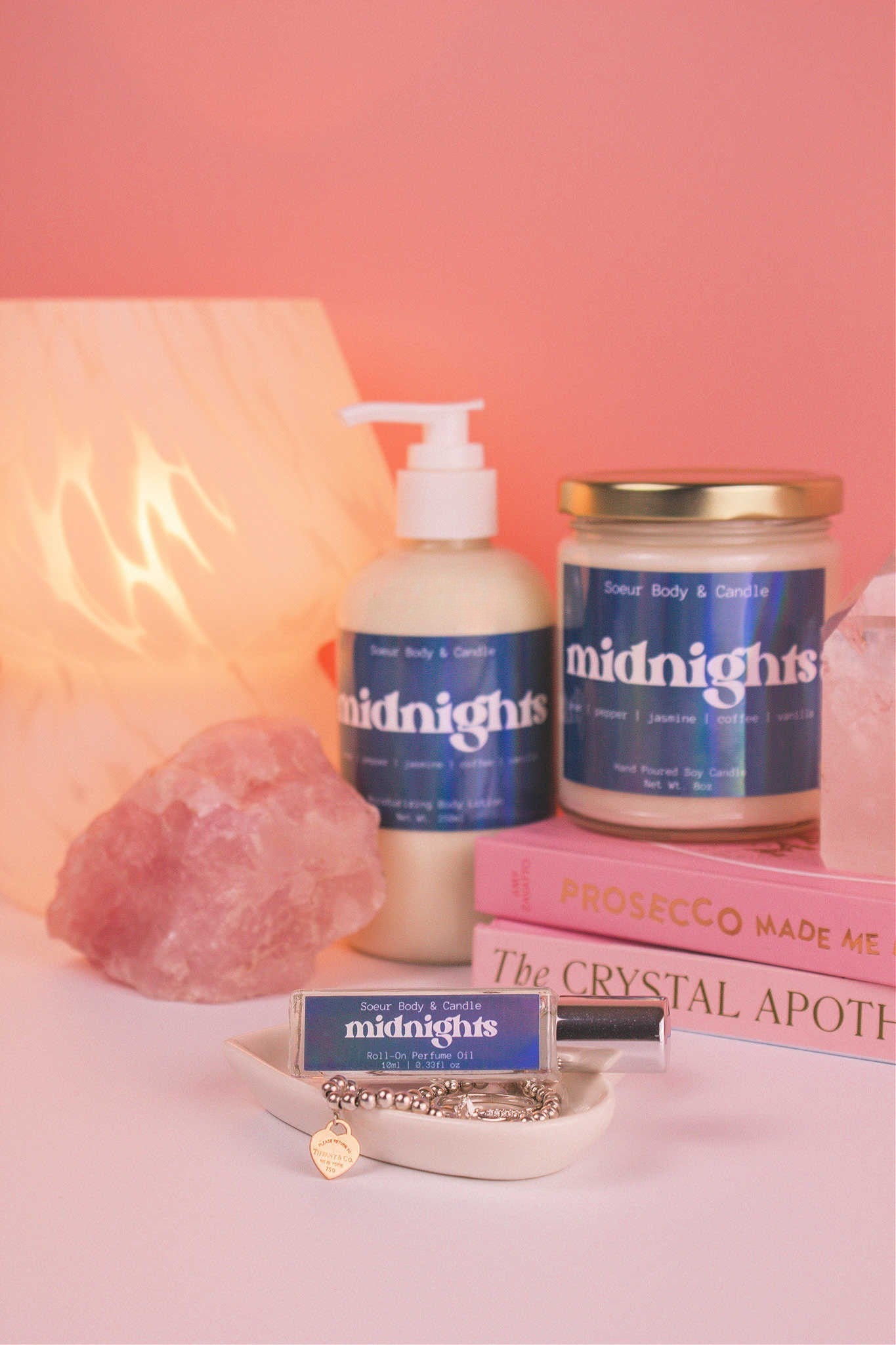 Midnights roll-on perfume in the foreground, with matching lotion and candle softly blurred in the background. Featuring bold notes of almond, coffee, jasmine, tonka bean, and cocoa.