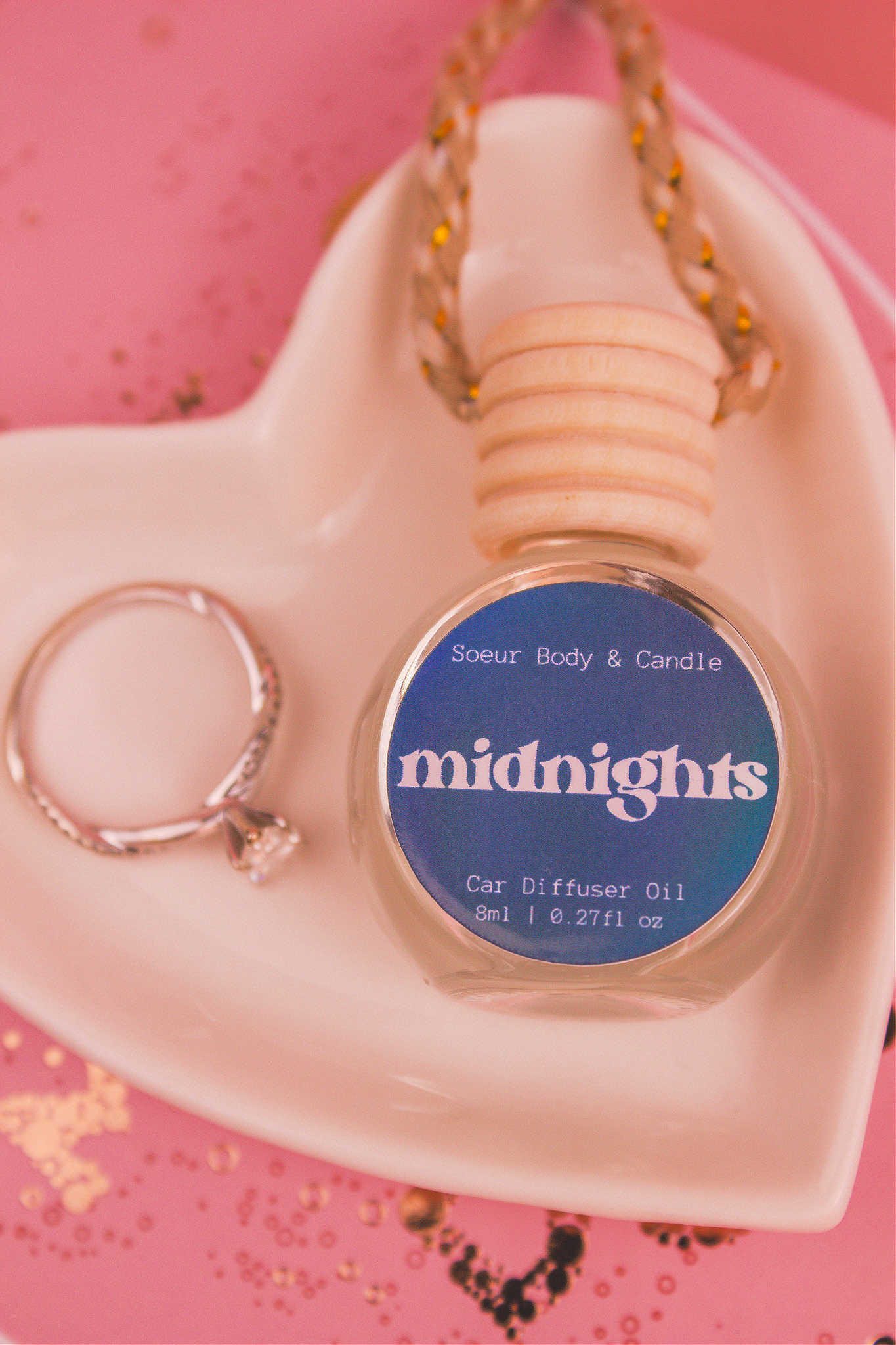 Close-up of Midnights car diffuser in a jewelry dish with a ring beside it, featuring an exotic blend of pear, pepper, jasmine, coffee, and vanilla notes.
