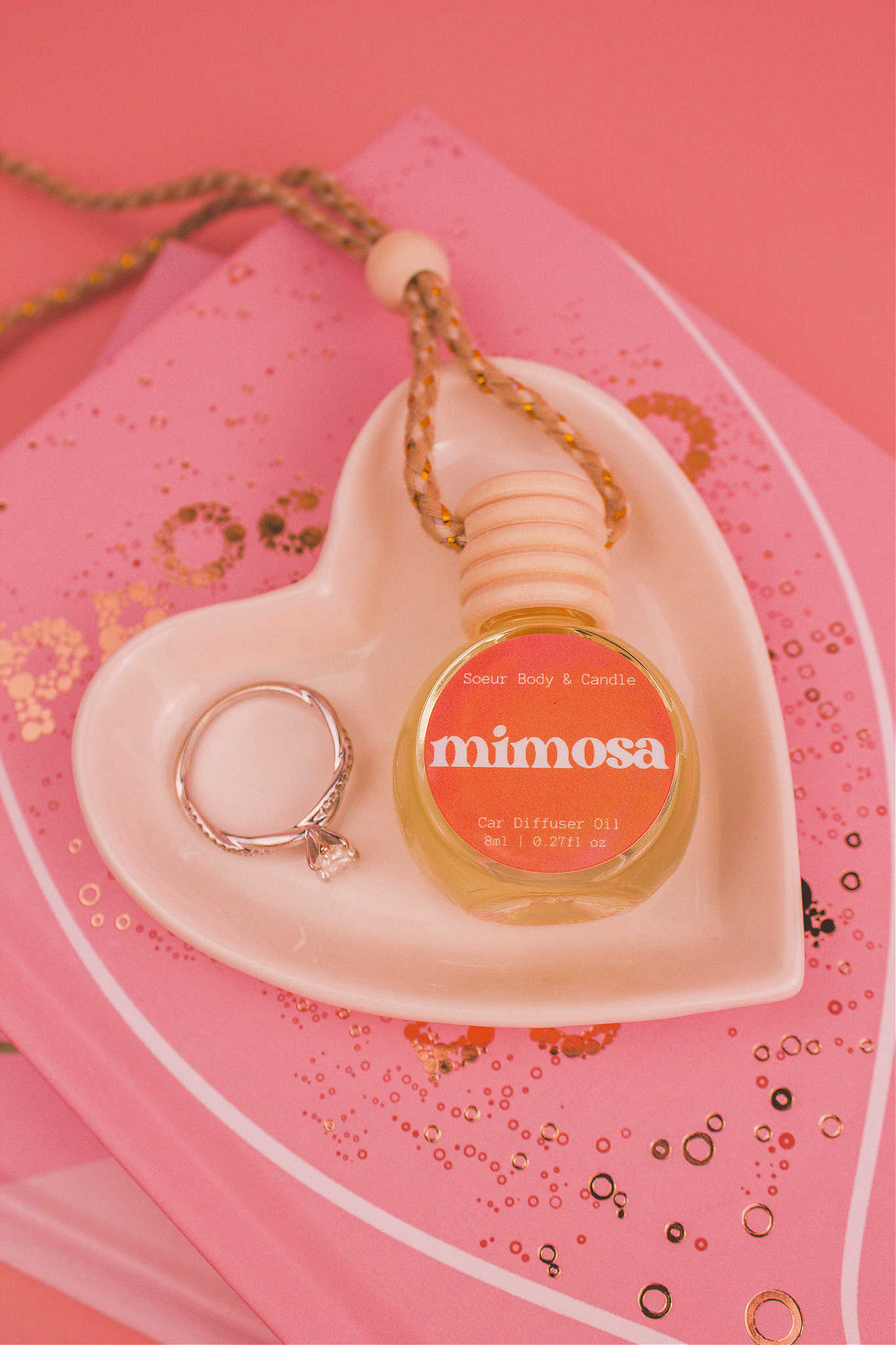 Mimosa car diffuser in a jewelry dish with a ring beside it, sitting on top of books, featuring a blend of orange, neroli, honeysuckle, and vanilla.