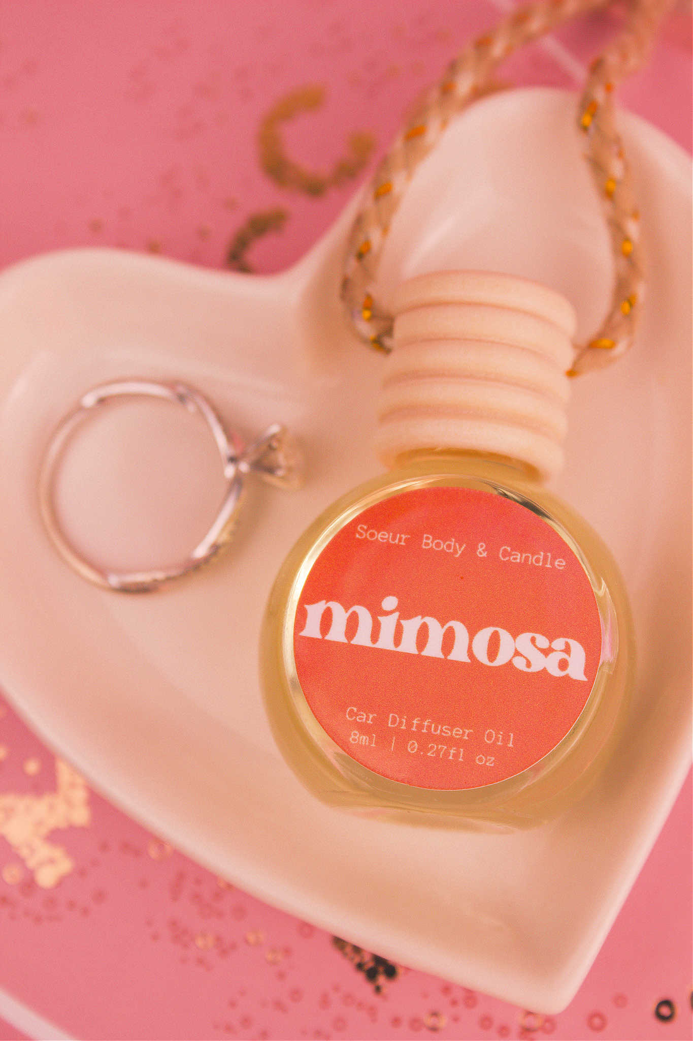 Close-up of Mimosa car diffuser in a jewelry dish with a ring beside it, featuring a blend of orange, neroli, honeysuckle, and vanilla.