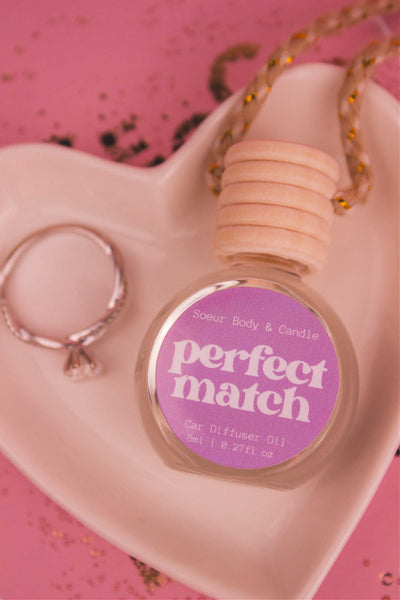 Close-up of Perfect Match car diffuser in a jewelry dish with a ring beside it, featuring notes of cherry, almond, jasmine, rose, and vanilla.