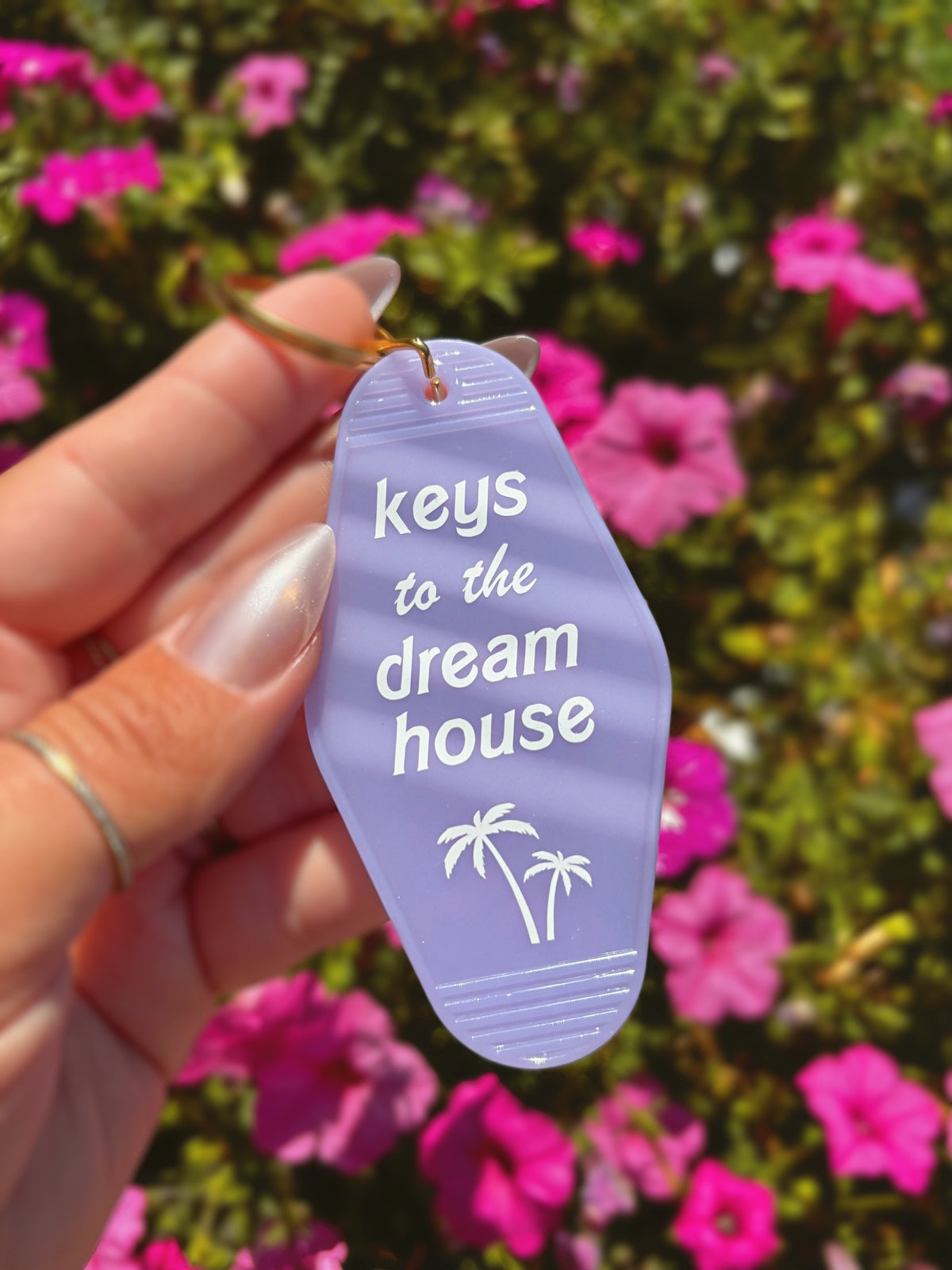 A hand holding a lavender flip-flop-shaped keychain with the text &