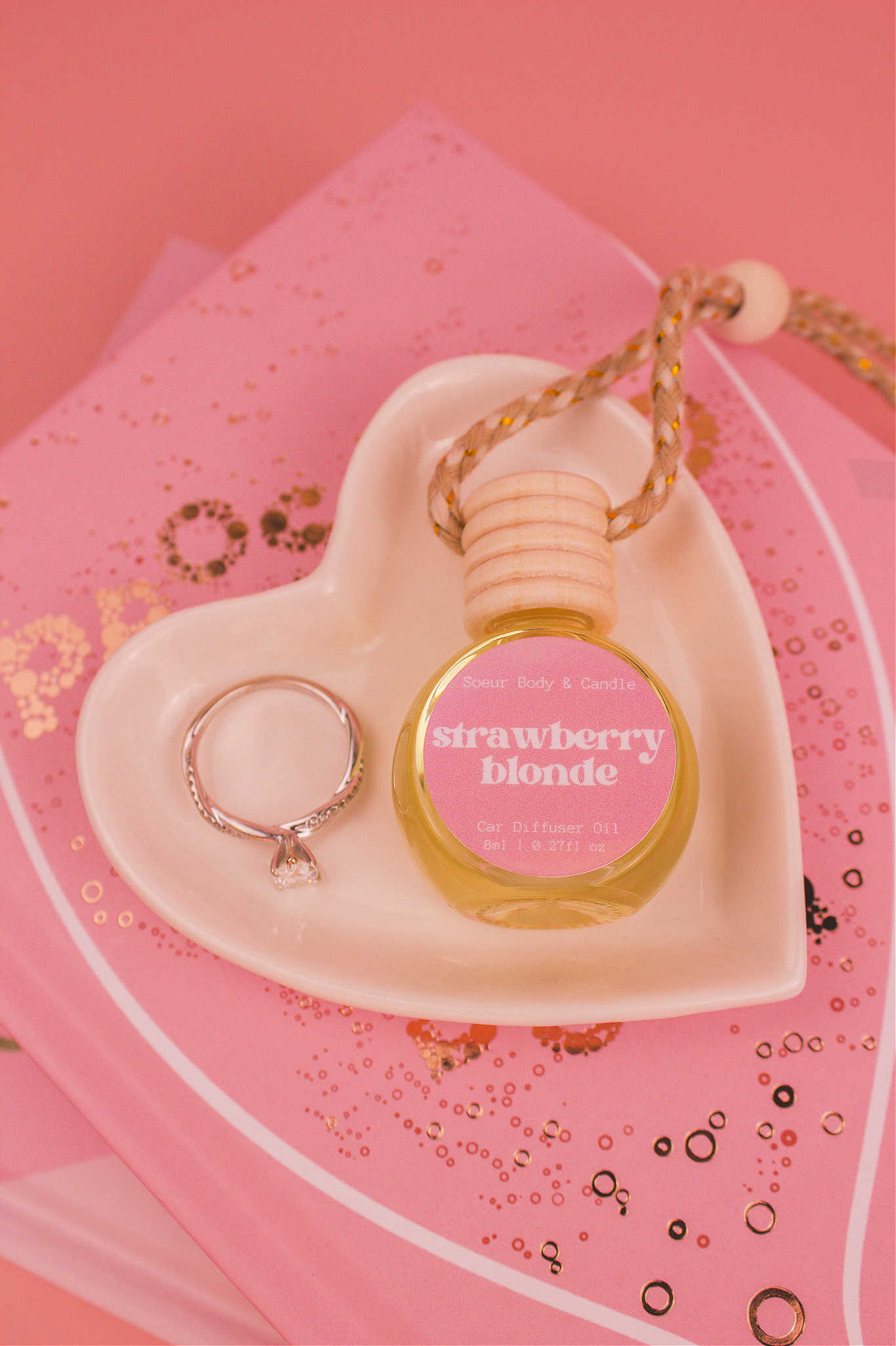 Strawberry Blonde car diffuser in a jewelry dish with a ring beside it, sitting on top of books. Featuring a delicious blend of sweet strawberry, sugar, and vanilla.