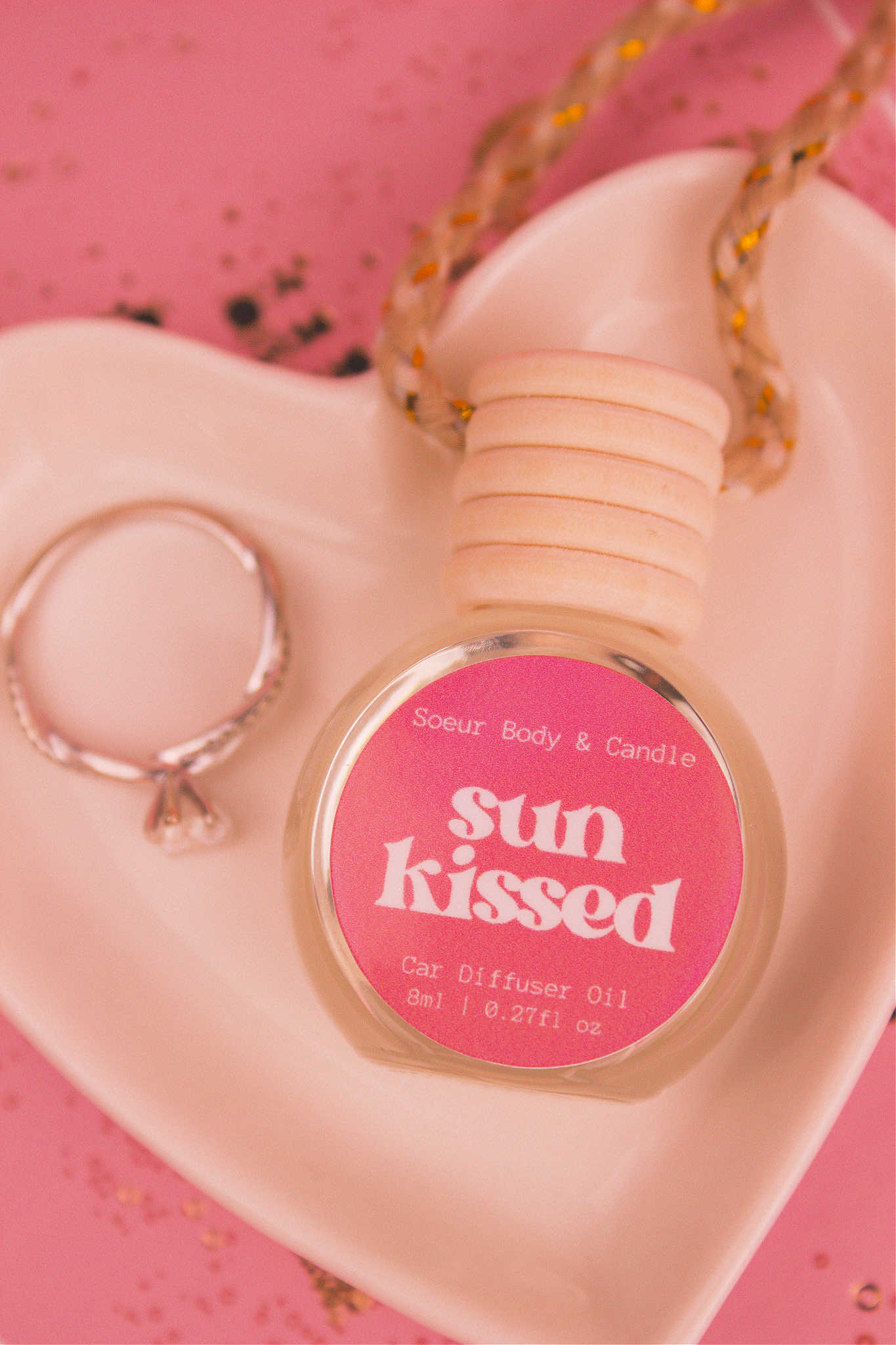 Close-up of Sun Kissed car diffuser in a jewelry dish with a ring beside it, featuring notes of salted caramel, pistachio, almond, and vanilla.