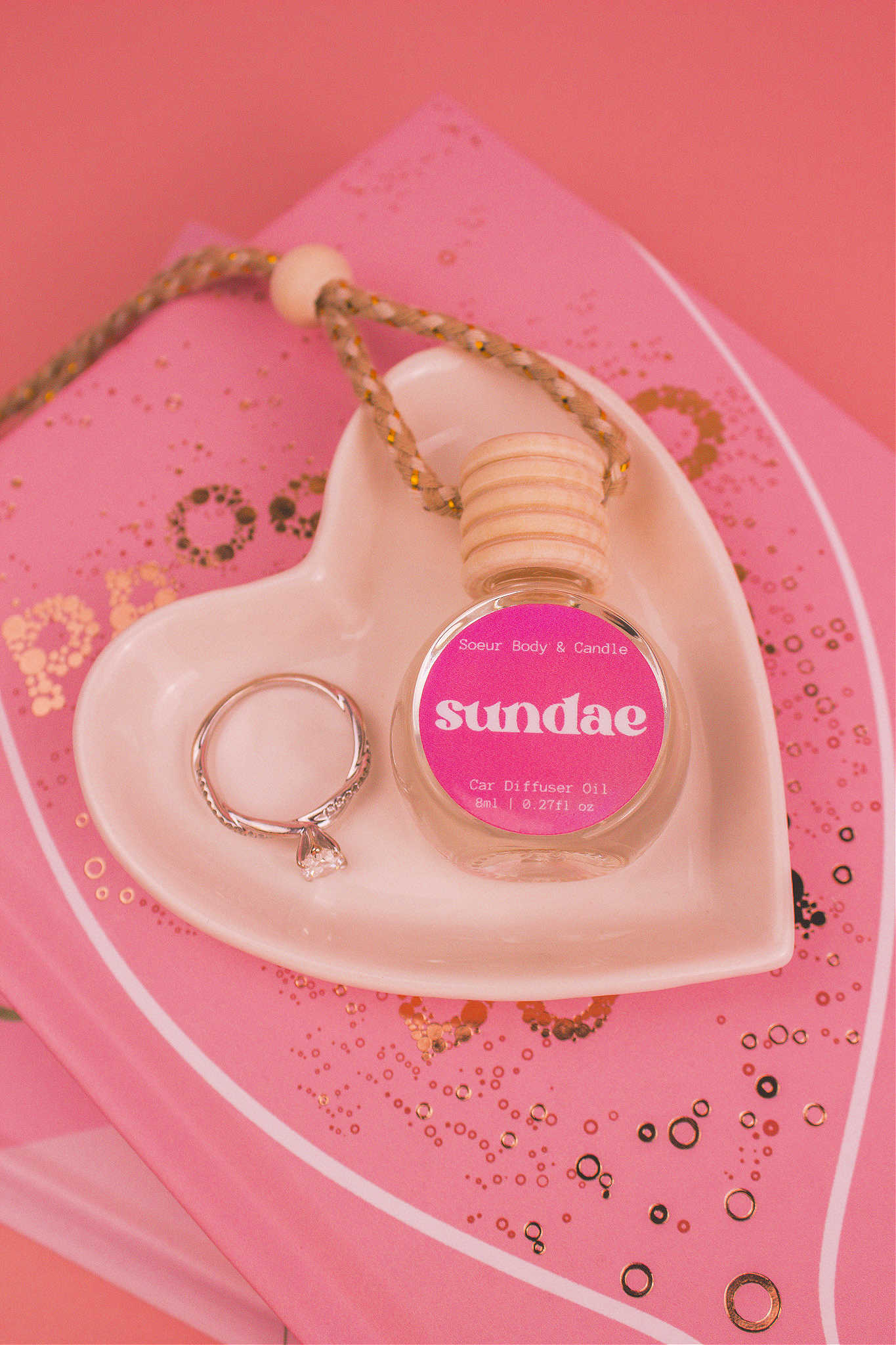 Sundae car diffuser in a jewelry dish with a ring beside it, sitting on top of books, featuring notes of sweet cream, vanilla, and sugary waffle cone.