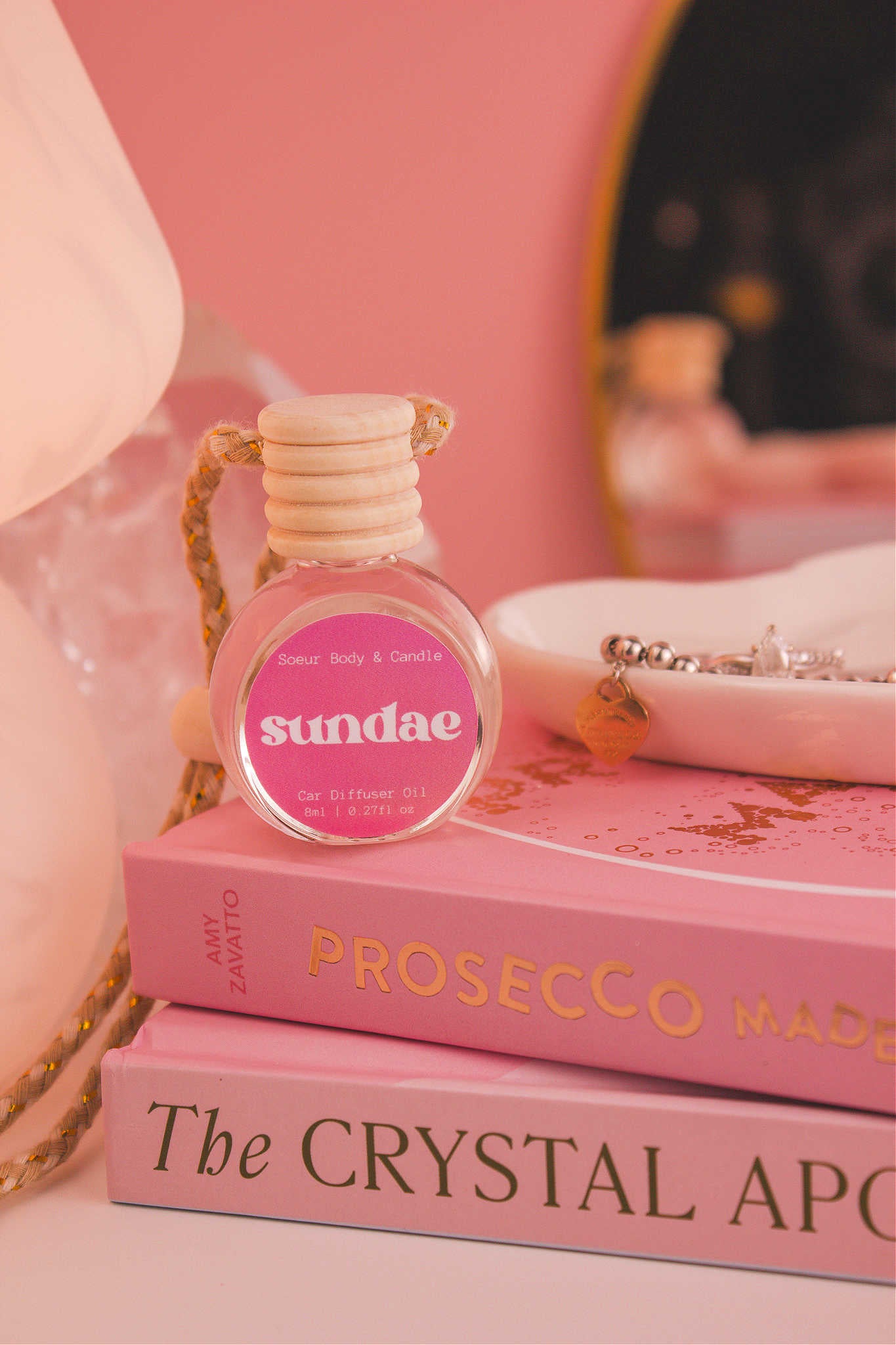 Sundae diffuser sitting on top of a stack of books with a jewelry dish in the background, set against a lamp, mirror, and crystals; fragrance notes: sweet cream, vanilla, and sugary waffle cone.