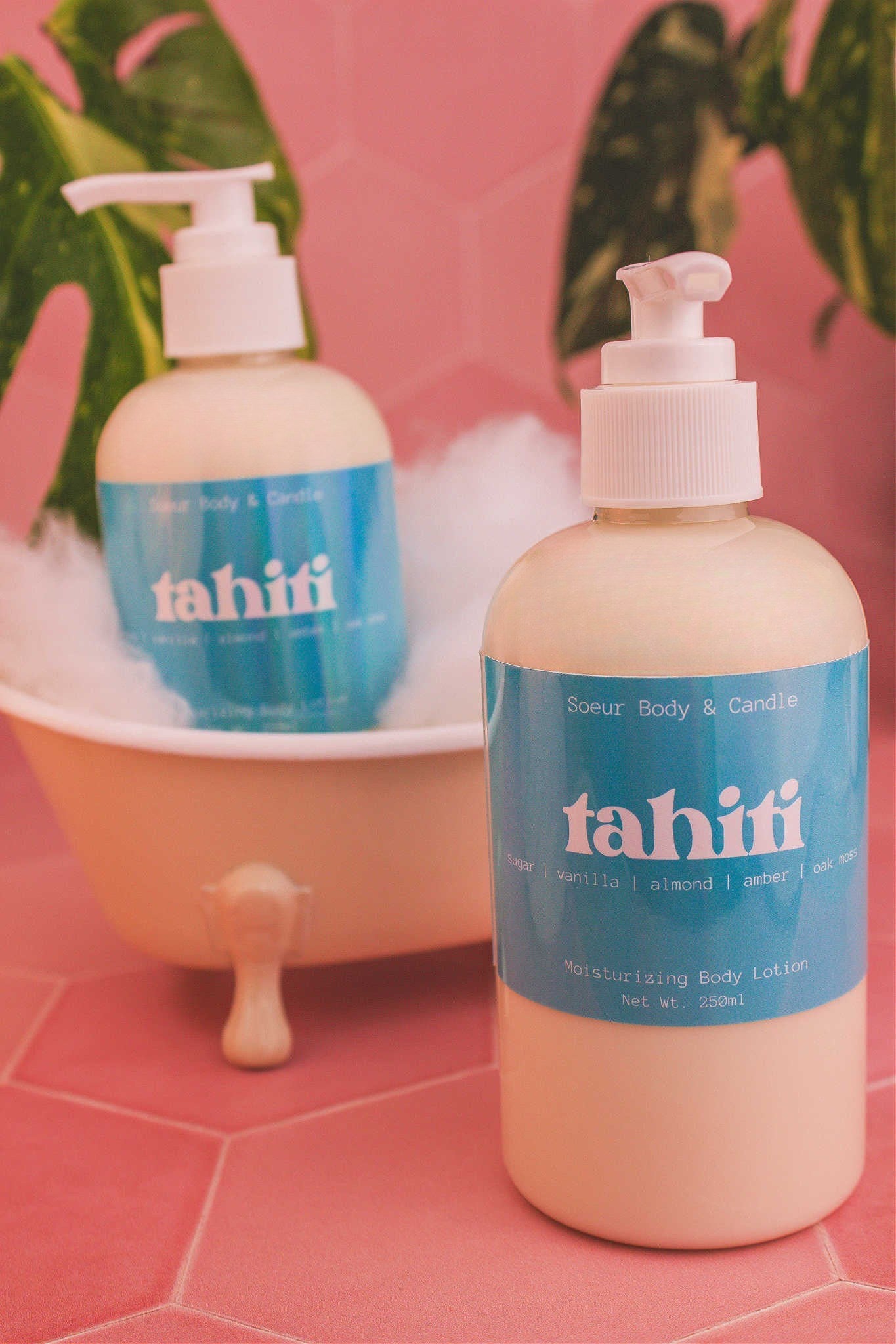 Display of two Tahiti body lotions in a small tub with bubbles and plants in the background, evoking a relaxing vibe with sugar, vanilla, almond, amber, and oak moss notes.