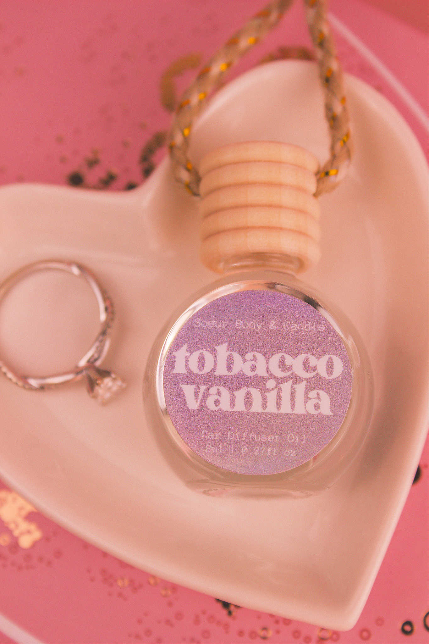 Close-up of Tobacco Vanilla car diffuser in a jewelry dish with a ring beside it, featuring notes of vanilla, amber, tobacco leaves, and tonka bean.