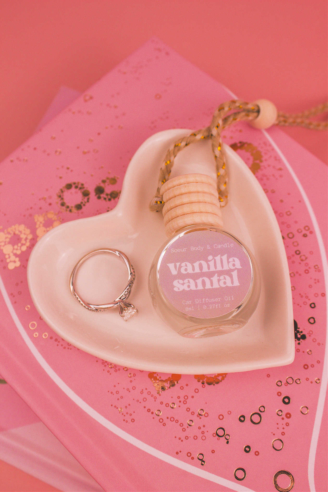 Vanilla Santal car diffuser in a jewelry dish with a ring beside it, sitting on top of books, featuring notes of shea butter, coconut, vanilla, and sandalwood.