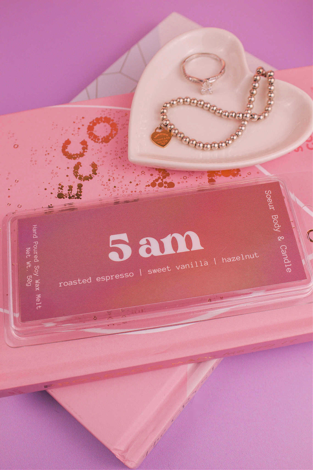 5am wax melt displayed on books with a jewelry dish and jewelry visible in the background, showcasing its roasted espresso, sweet vanilla, and hazelnut aroma.