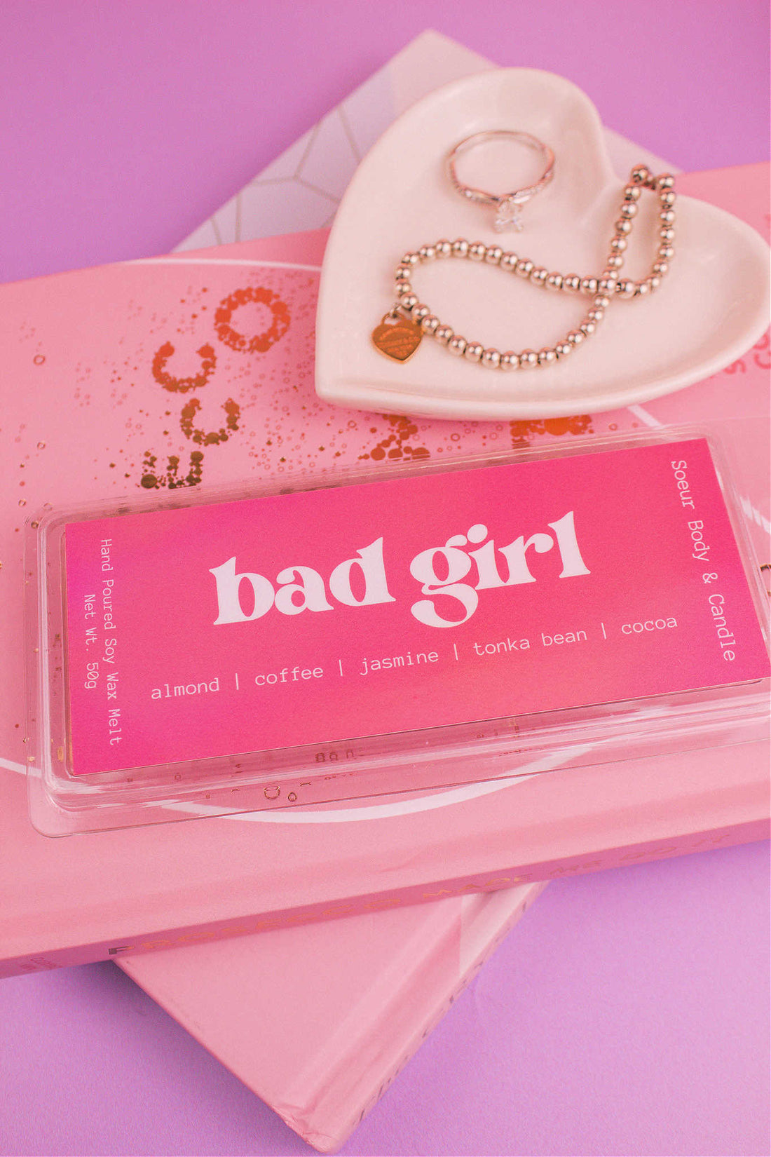 Bad Girl wax melt set on books with a jewelry dish and jewelry in view, highlighting its blend of almond, coffee, jasmine, tonka bean, and cocoa.