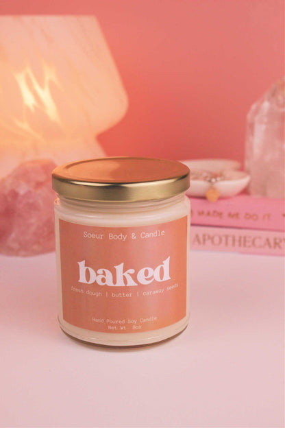 Baked candle with the lid on, with a stack of books and a jewelry dish in the background, set against a lamp and crystals; fragrance notes: fresh dough, butter, and caraway seeds.