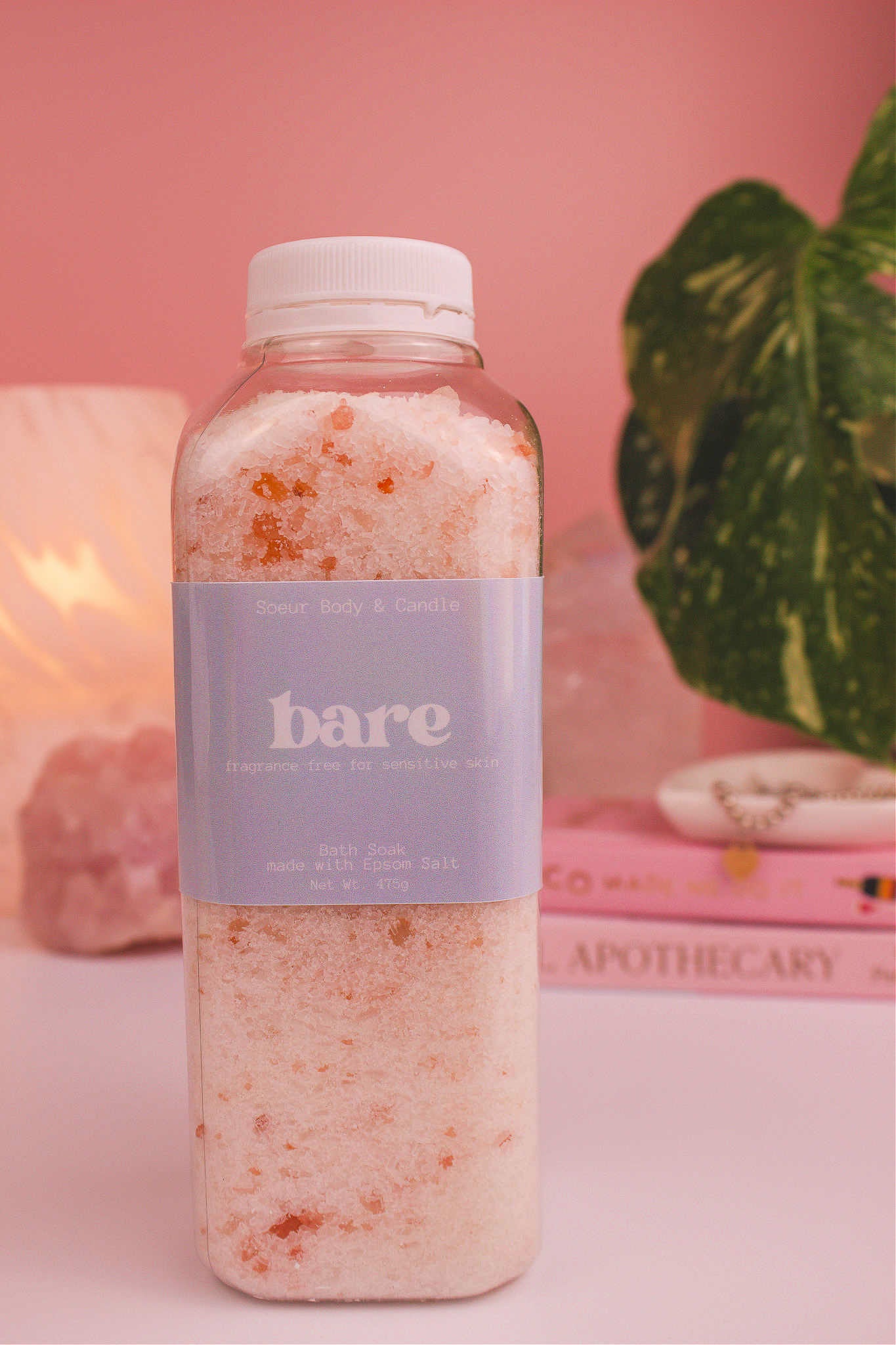 Bare bath soak with a stack of books, a jewelry dish, lamp, plants, and crystals in the background. Fragrance free for sensitive skin.