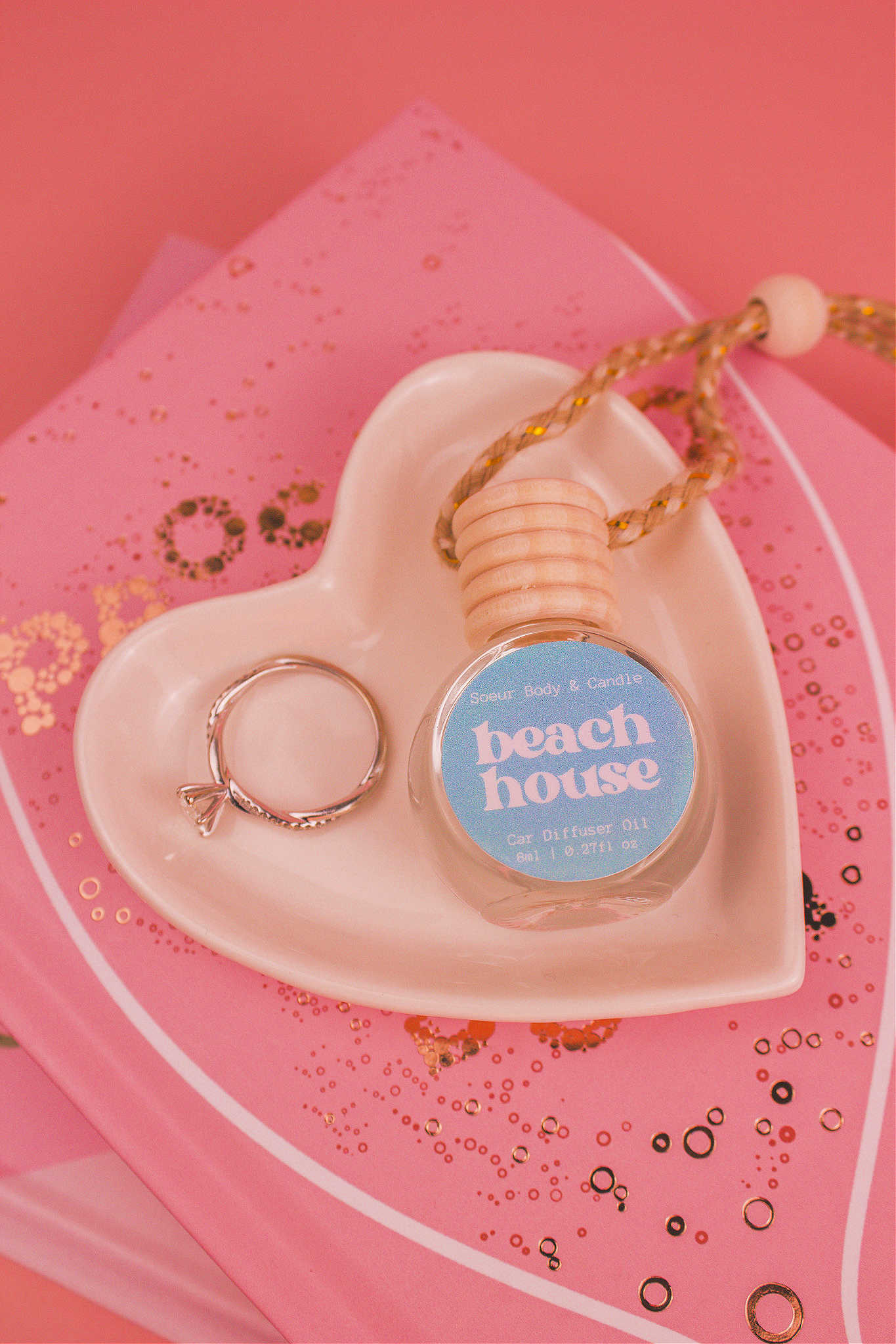 Beach House car diffuser in a jewelry dish with a ring beside it, sitting on top of books, featuring refreshing notes of citrus fruits, coconut, vanilla, and warm musk.