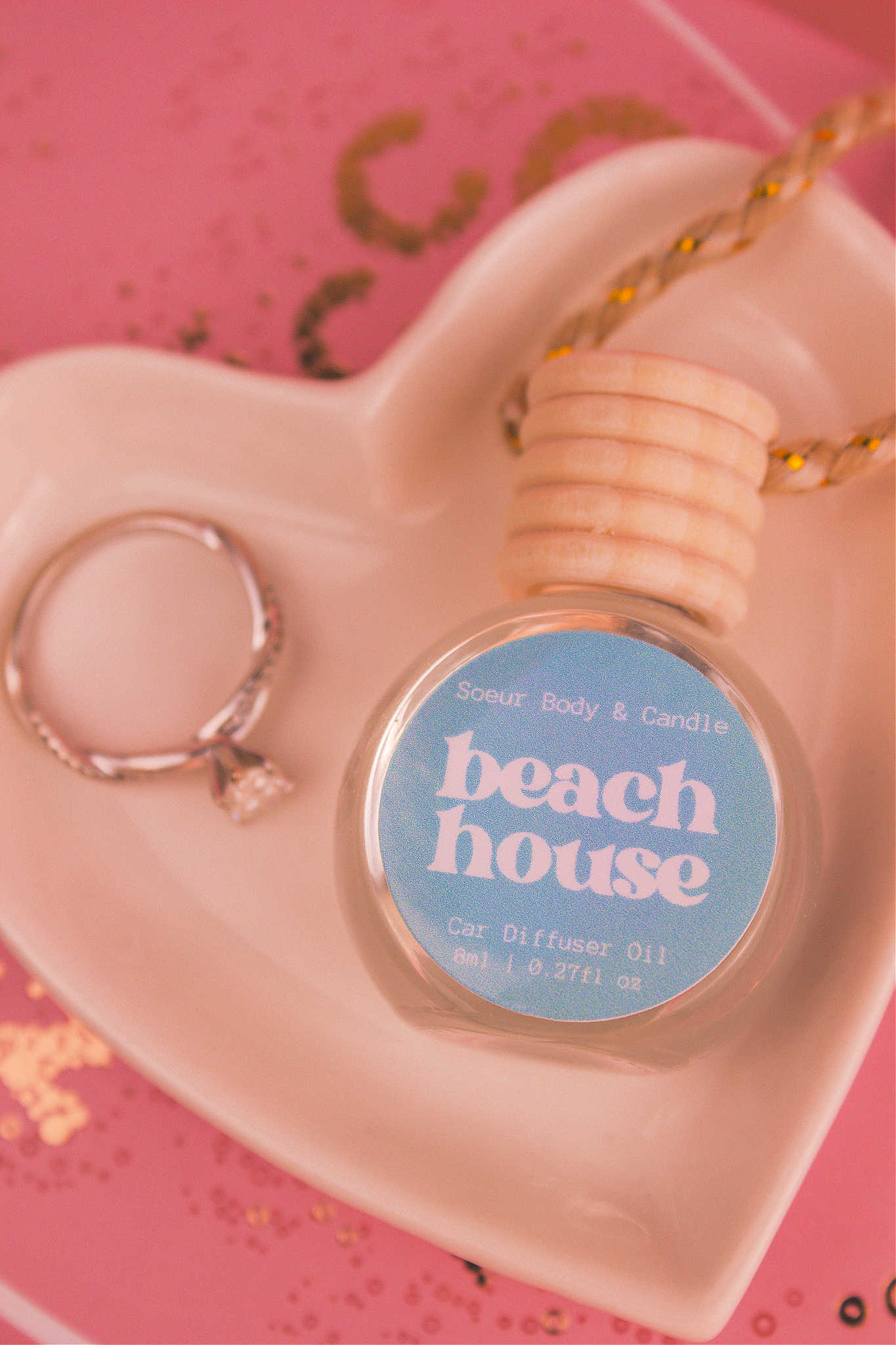 Close-up of Beach House car diffuser in a jewelry dish with a ring beside it, featuring refreshing notes of citrus fruits, coconut, vanilla, and warm musk.