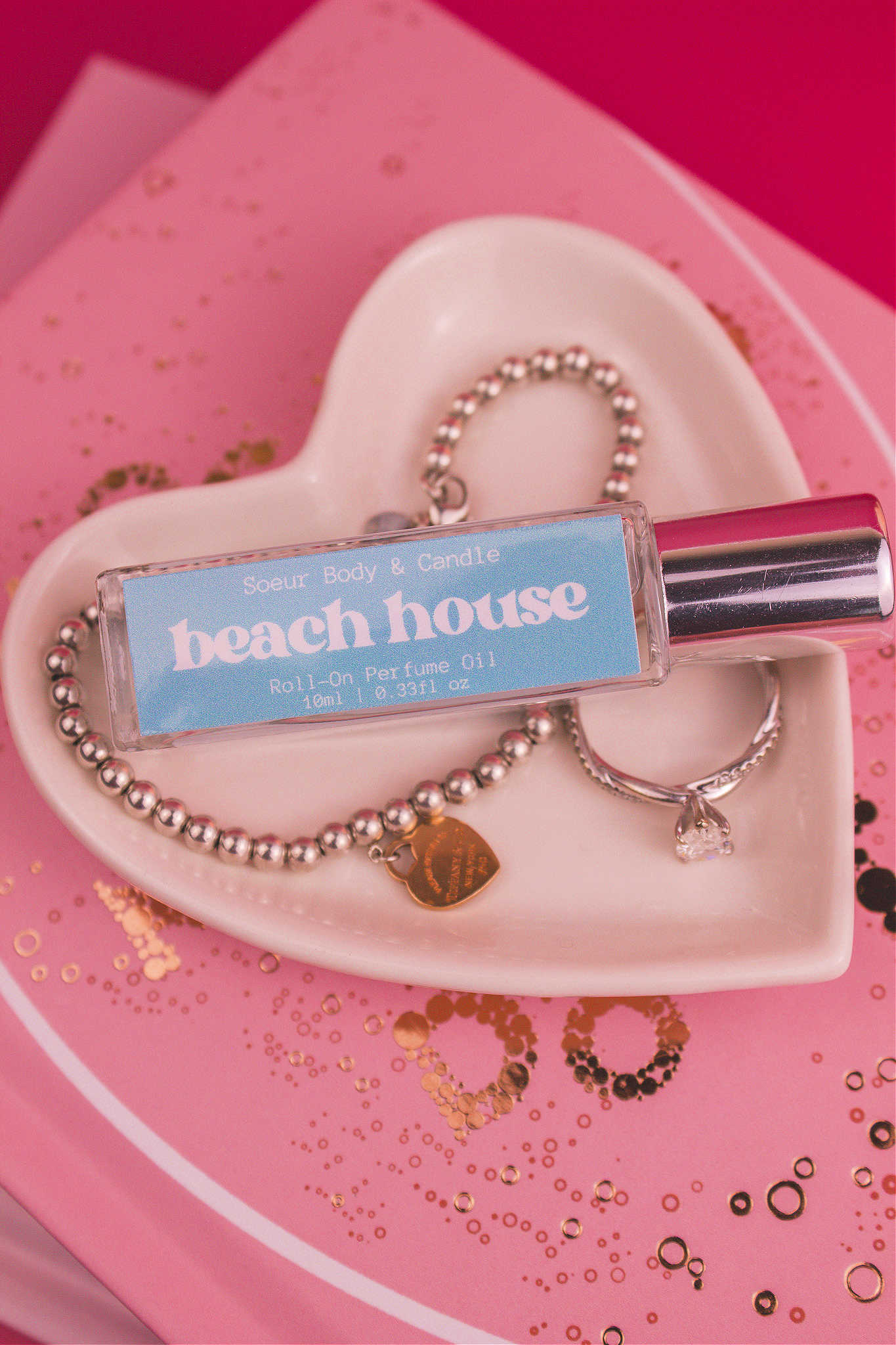 Beach House roll-on perfume bottle displayed in a jewelry dish beside a ring and bracelet, highlighting its vibrant citrus, coconut, vanilla, and warm musk aroma.