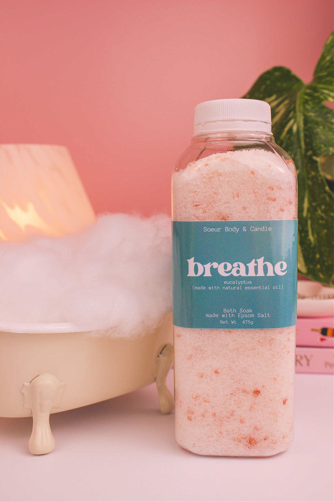 Breathe bath soak beside a small tub with bubbles, a lamp, and plants in the background, creating a relaxing vibe with eucalyptus essential oil.