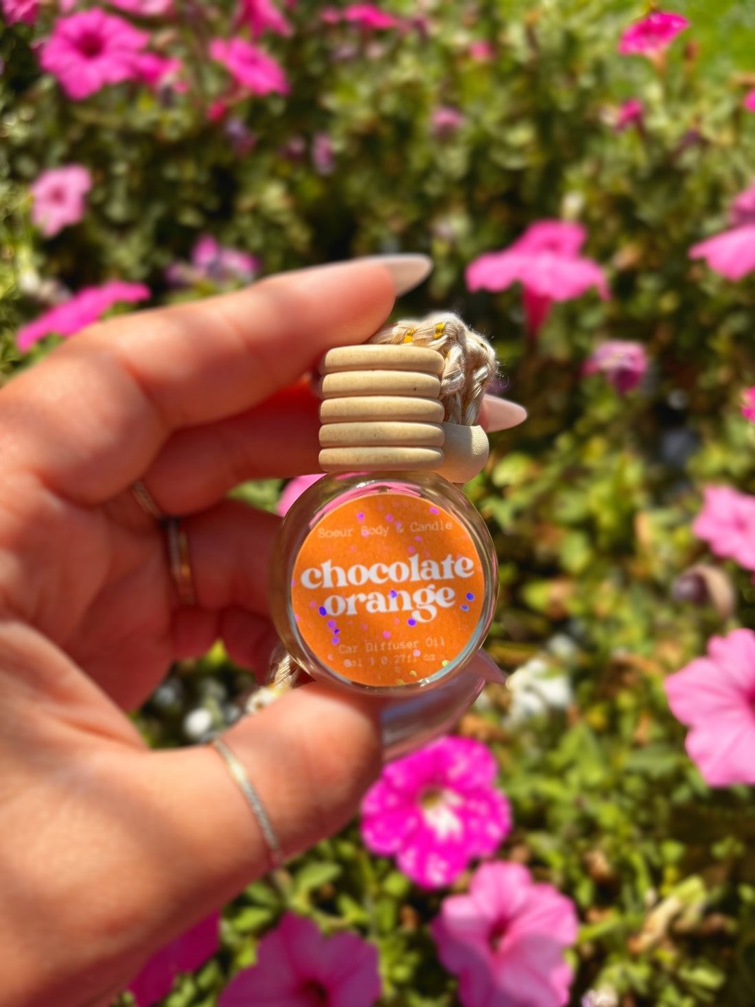A hand holding a round car diffuser labeled &
