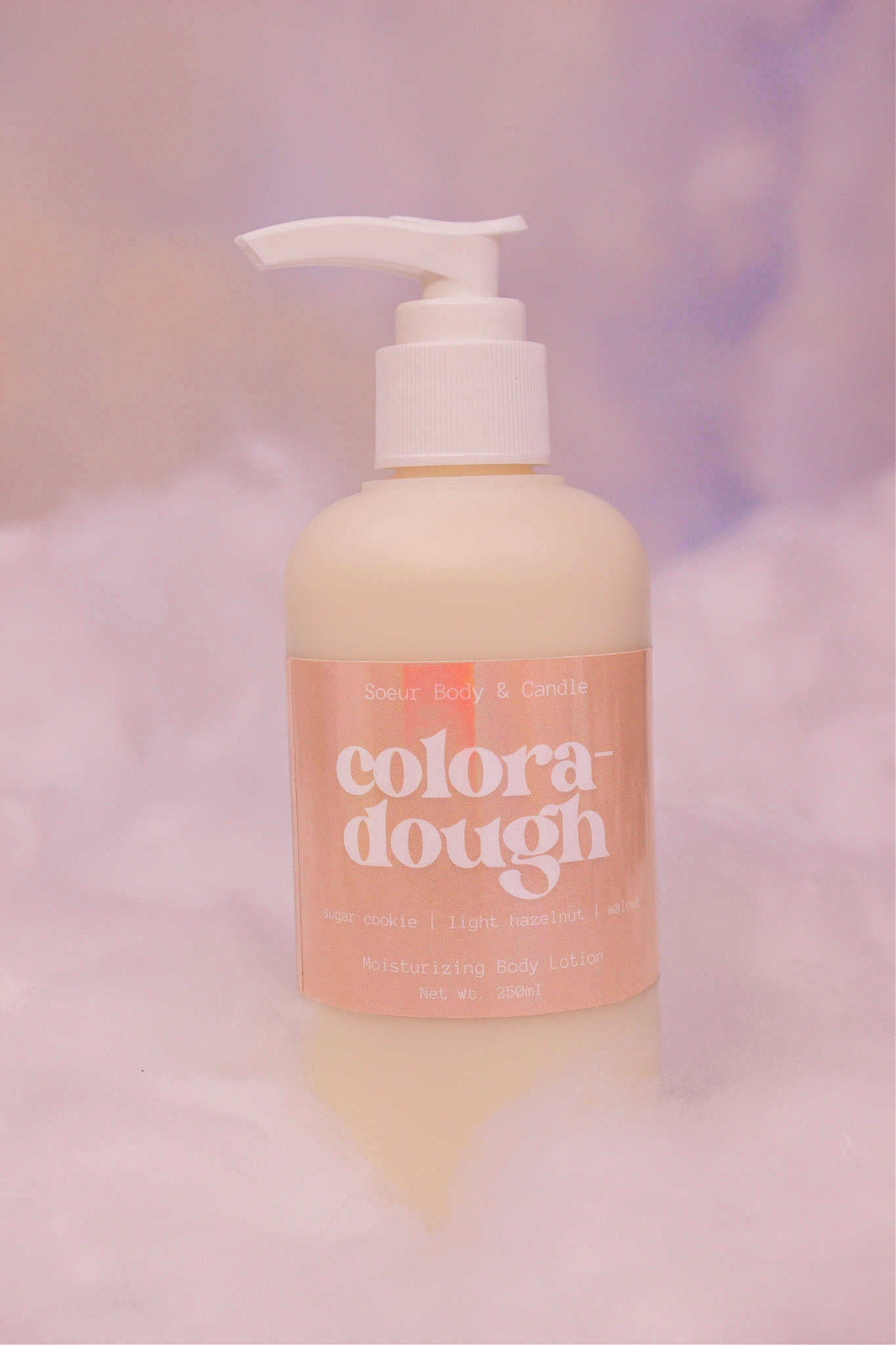 Coloradough body lotion sitting in fake snow against a cloudy background. Featuring notes of sugar cookie, light hazelnut, and walnut.