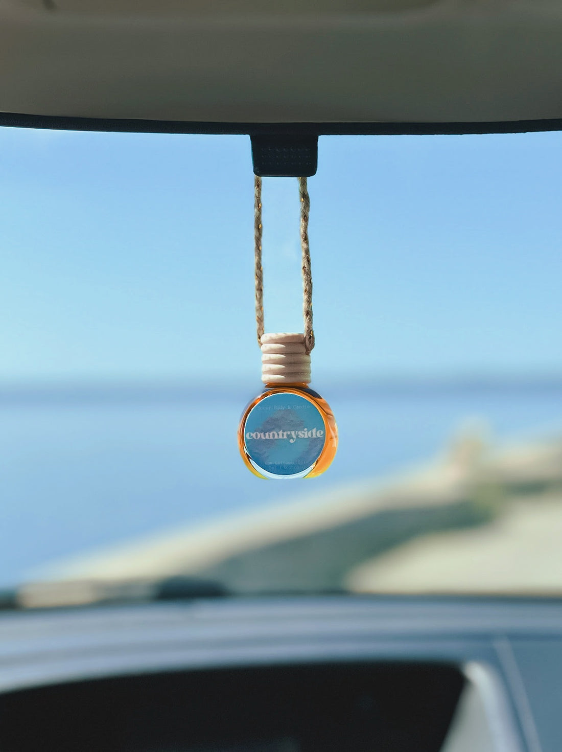 Countryside Diffuser Oil hanging from a rearview mirror, offering a balanced, long-lasting fragrance of blueberry, sugar, butter, cinnamon, and vanilla. Perfect for cars, closets, lockers, and more.