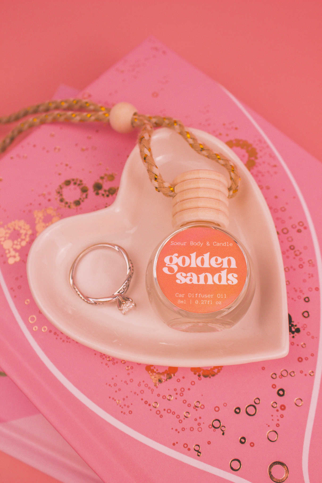 Golden Sands car diffuser in a jewelry dish with a ring beside it, sitting on top of books, featuring fresh air, lemon, sandalwood, and vanilla notes.