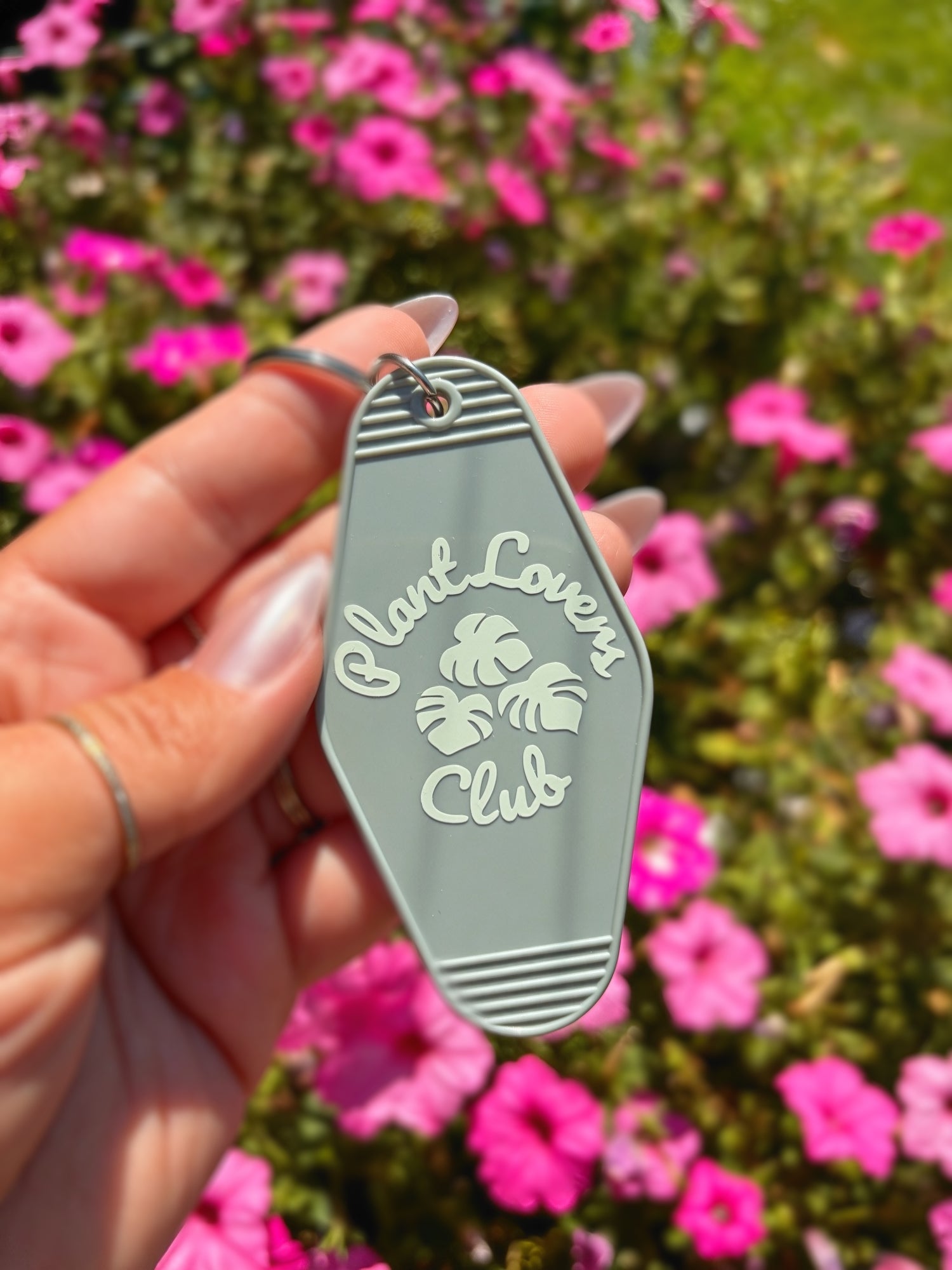 A hand holding a sage green plastic keychain with the words &