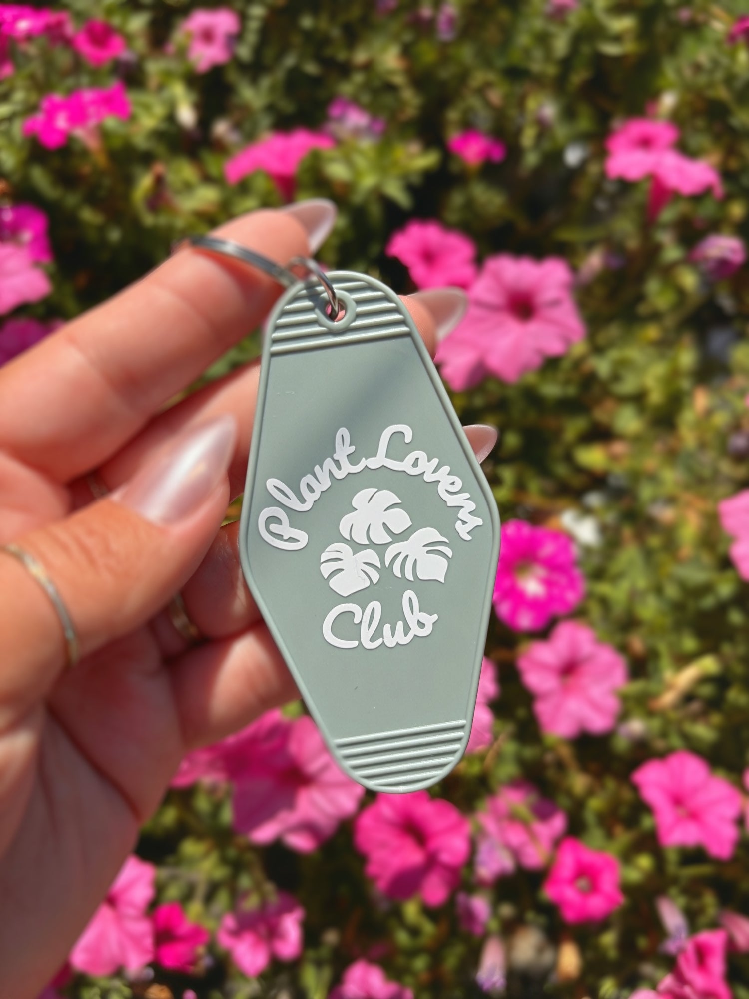 A hand holding a light sage green keychain with white text reading &