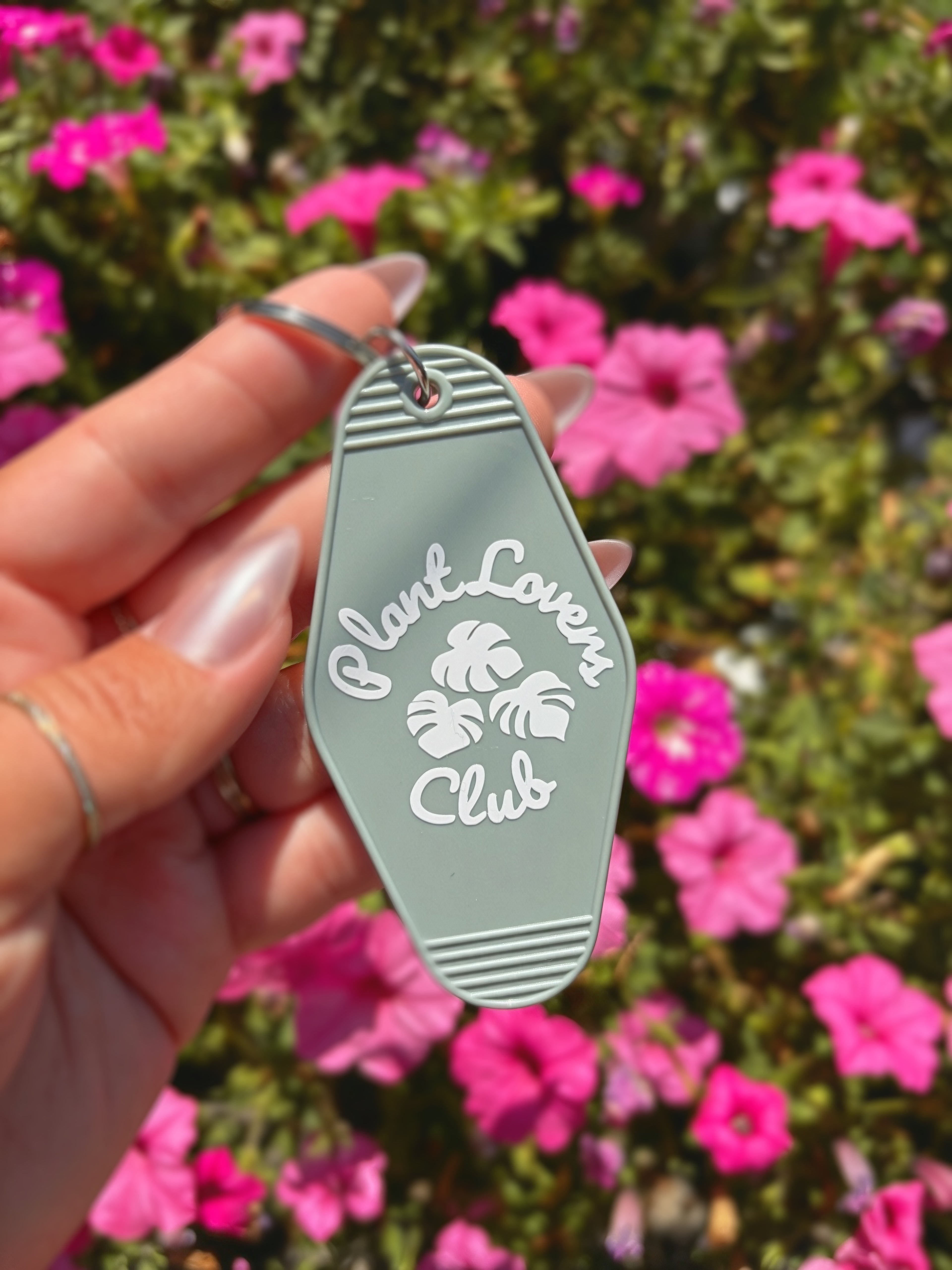 A hand holding a light sage green keychain with white text reading &