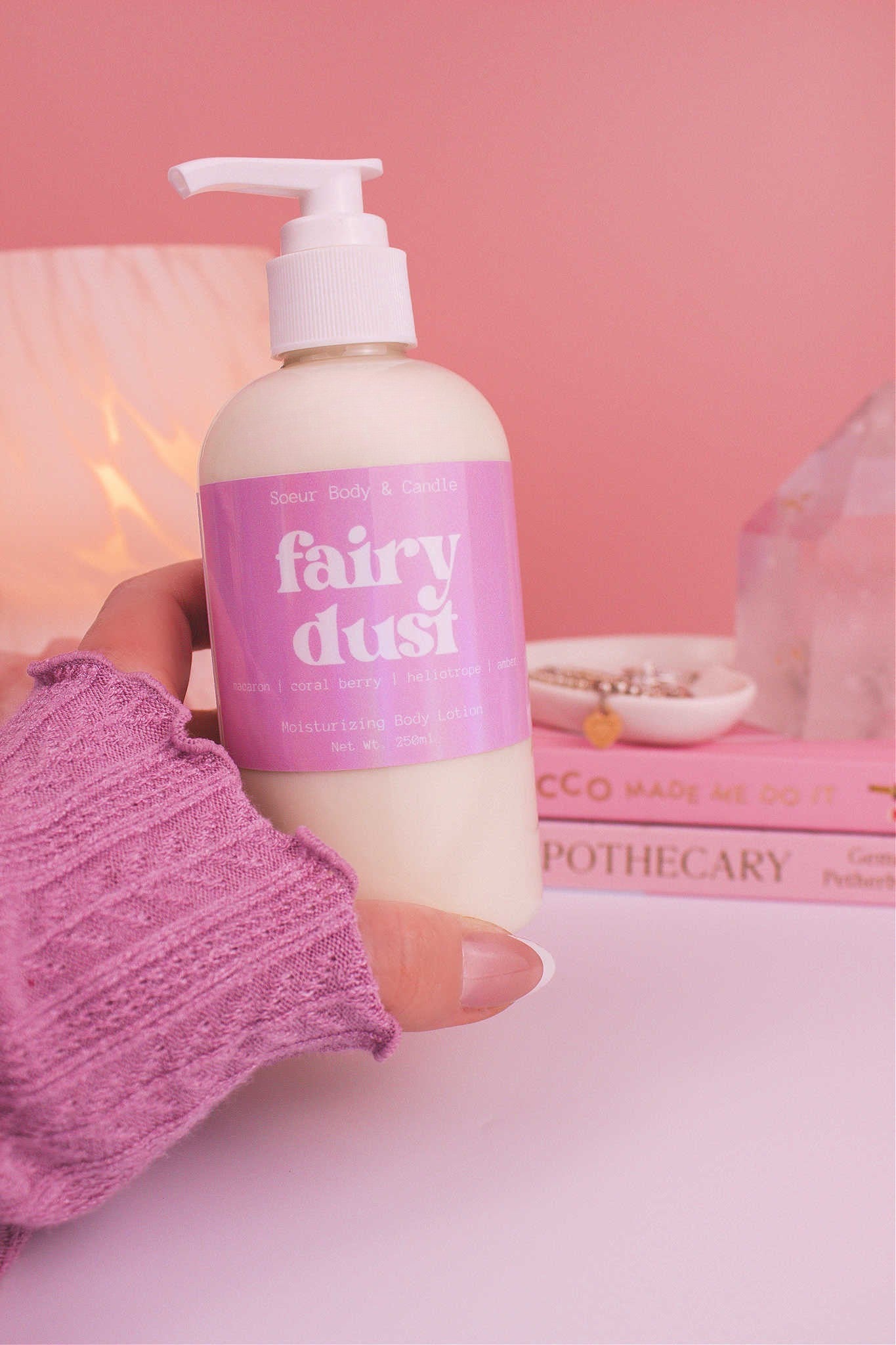 Close-up of a hand holding the Fairy Dust body lotion, highlighting its luxurious texture and sweet scent of macaron, coral berry, heliotrope, and amber.