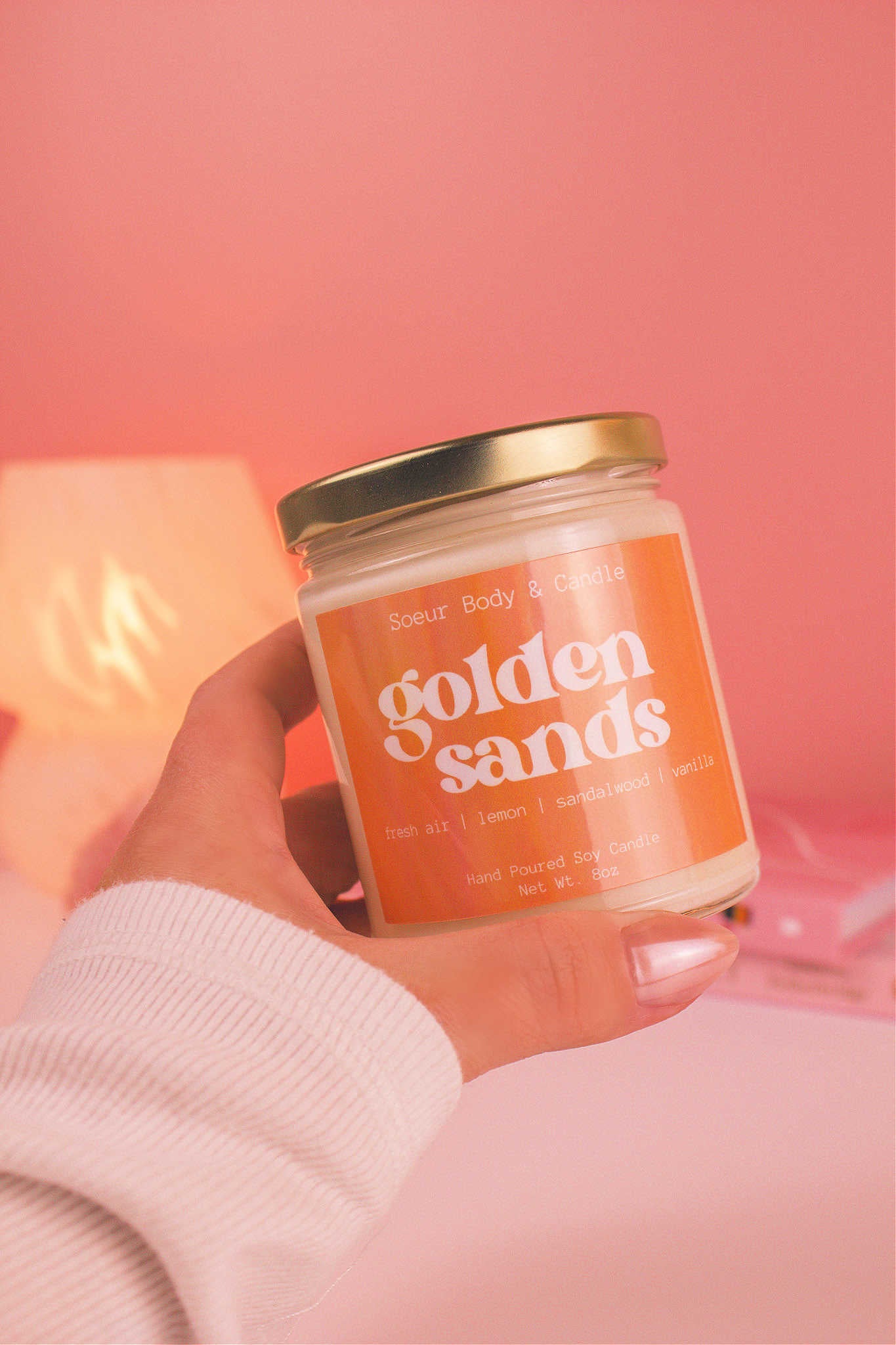 Close-up of a hand holding the Golden Sands candle, showcasing its design and fragrance notes of fresh air, lemon, sandalwood, and vanilla.