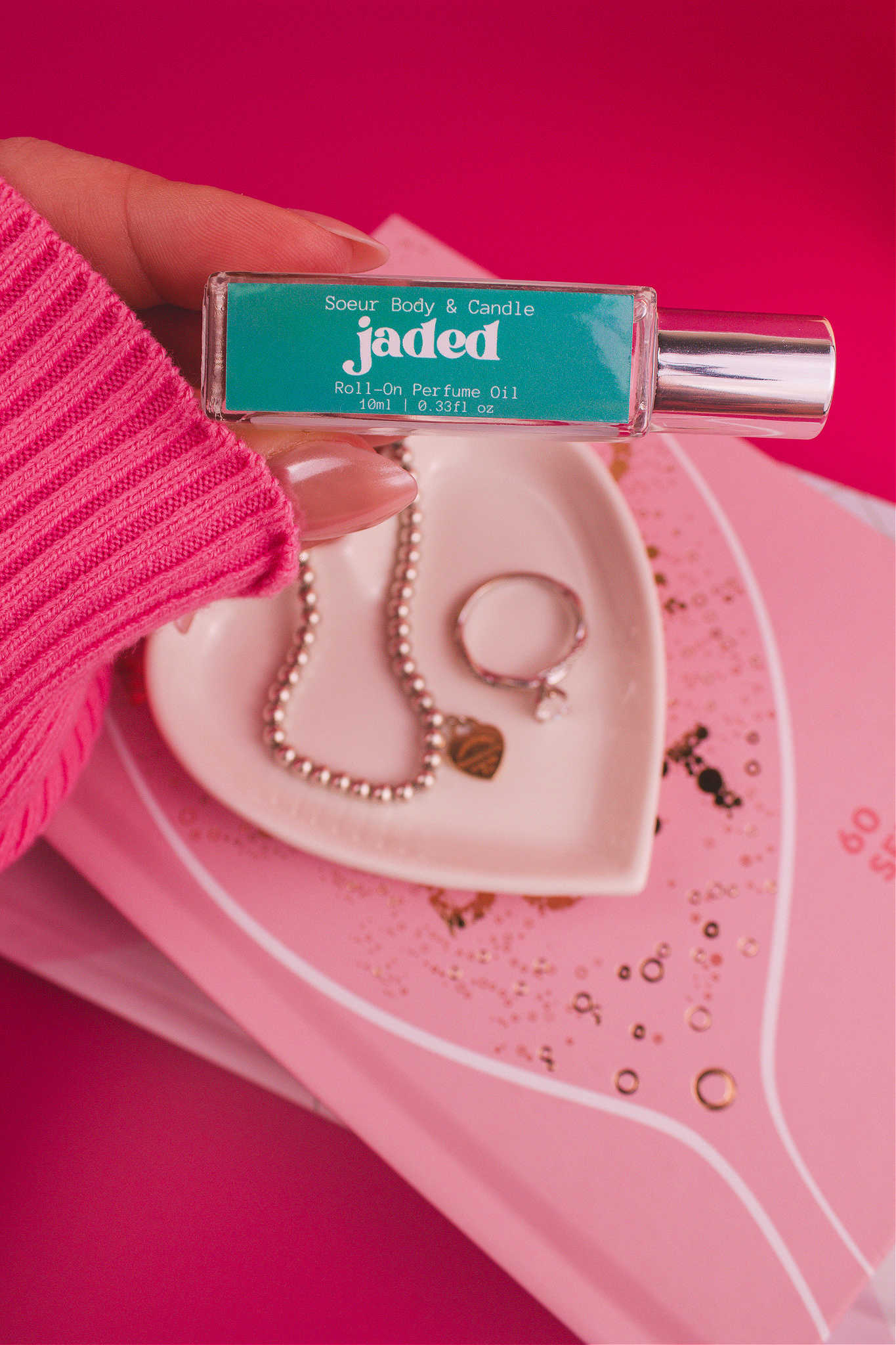 Close-up shot of Jaded roll-on perfume held in hand with a jewelry dish and jewelry in the background, capturing its layered blend of spruce, pine, amber, vetiver, and musk.