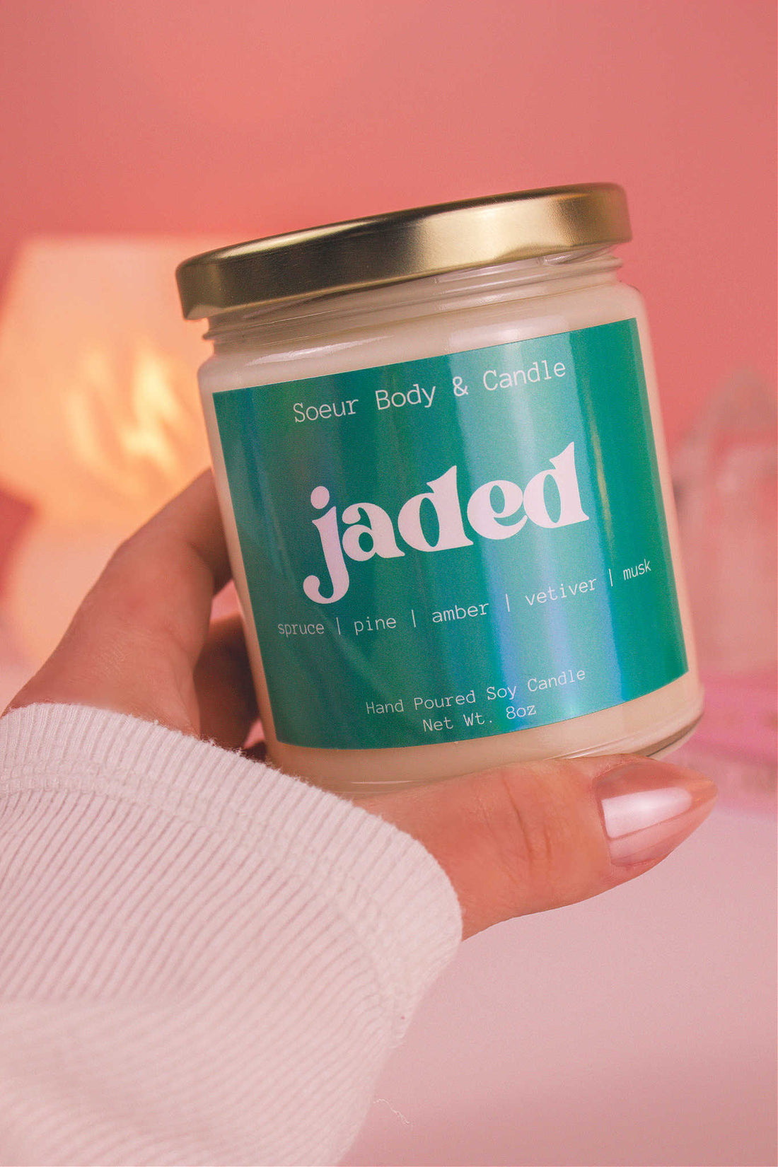 Close-up of a hand holding the Jaded candle, showcasing its design and fragrance notes of spruce, pine, amber, vetiver, and musk.