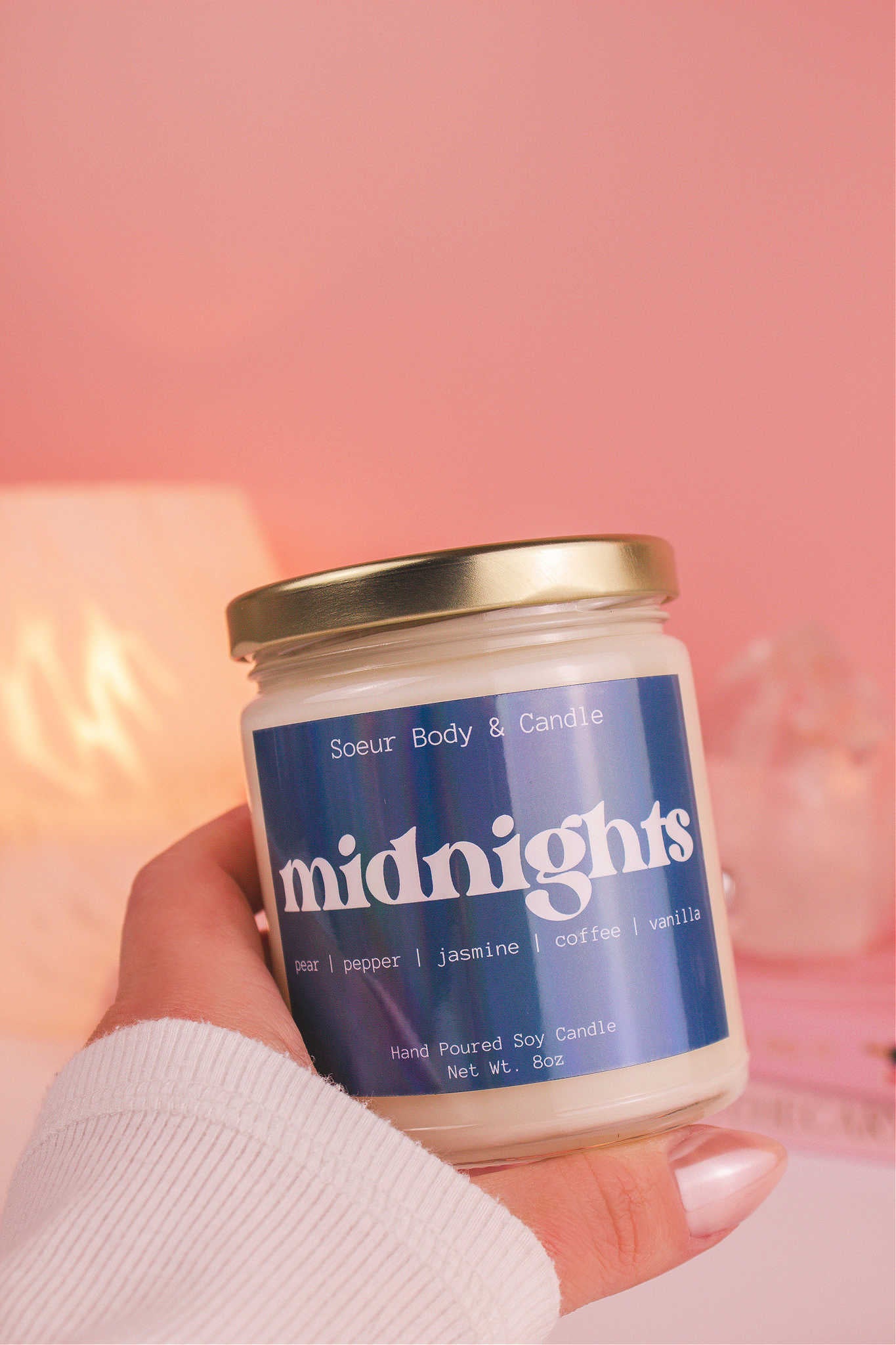 Close-up of a hand holding the Midnights candle, showcasing its design and fragrance notes of pear, pepper, jasmine, coffee, and vanilla.