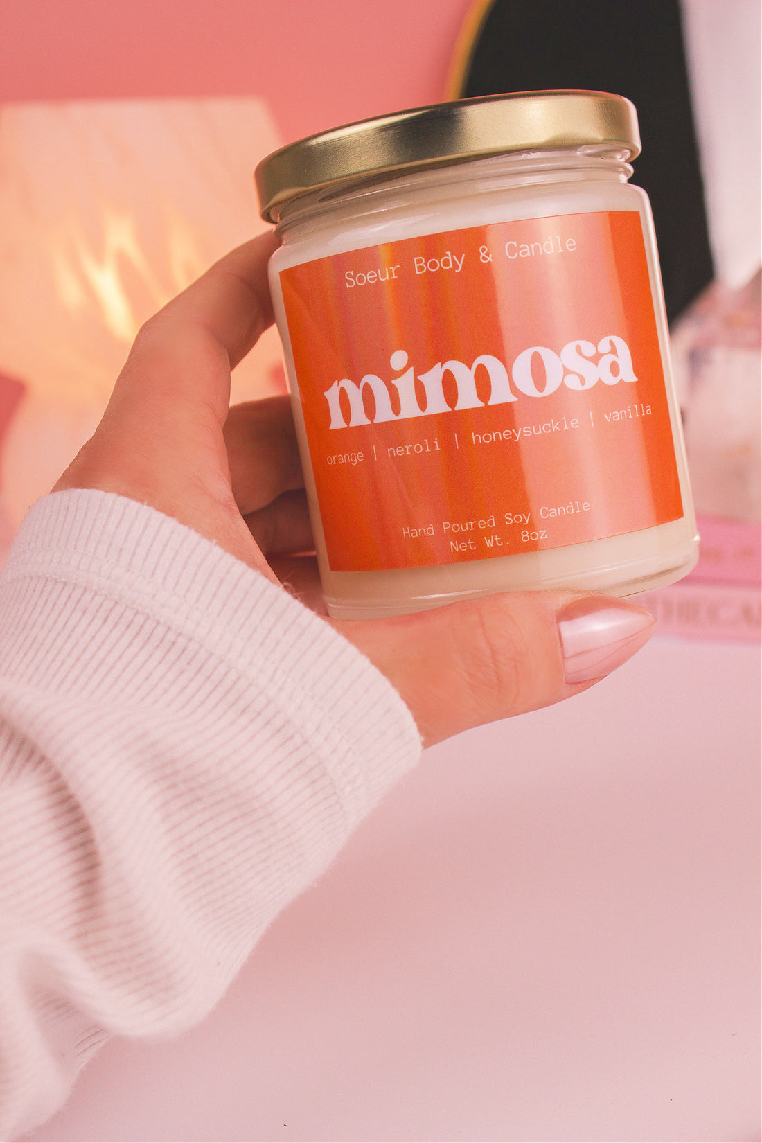 Close-up of a hand holding the Mimosa candle, showcasing its design and fragrance notes of orange, neroli, honeysuckle, and vanilla.