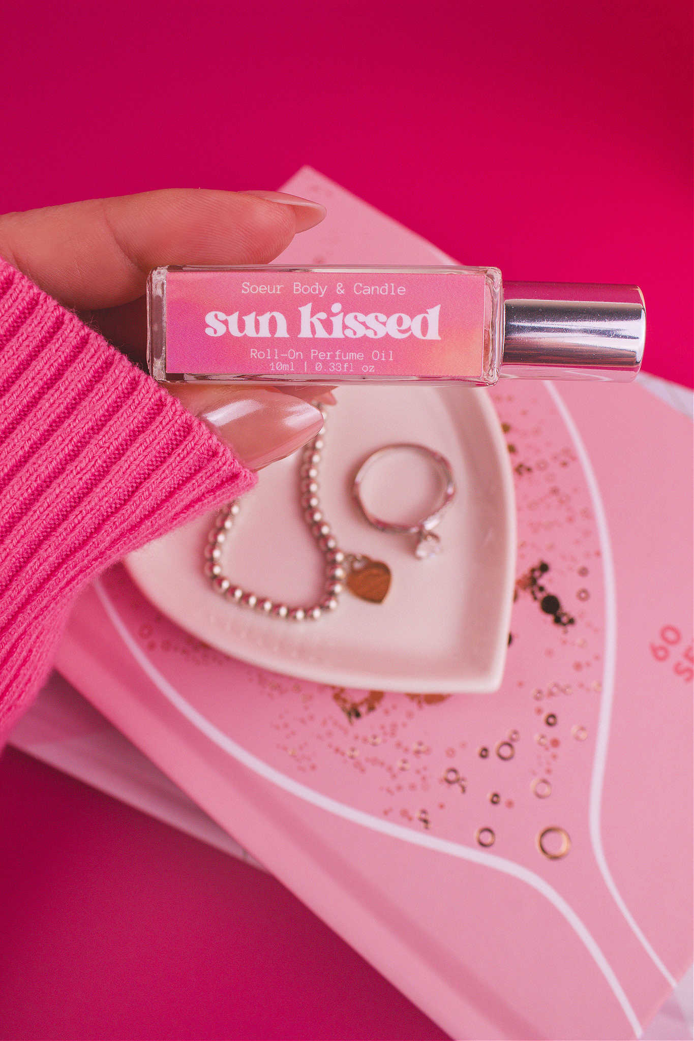 Close-up shot of Sun Kissed roll-on perfume held in hand with a jewelry dish and jewelry in the background, capturing its layered blend of salted caramel, pistachio, almond, and vanilla.