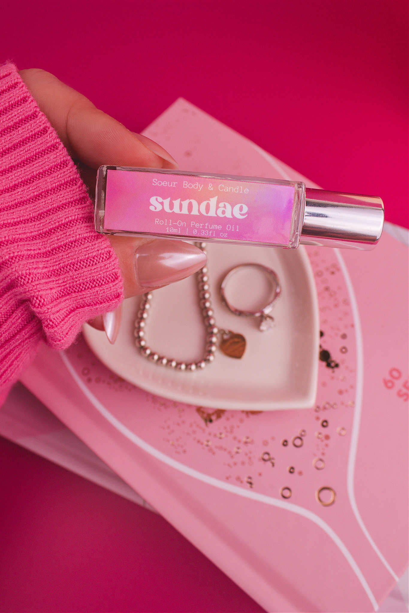 Close-up shot of Sundae roll-on perfume held in hand with a jewelry dish and jewelry in the background, capturing its layered blend of sweet cream, vanilla, and sugary waffle cone.