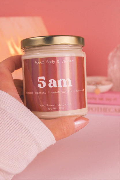 Close-up of a hand holding the 5am candle, showcasing its design and fragrance notes of roasted espresso, sweet vanilla, and hazelnut.