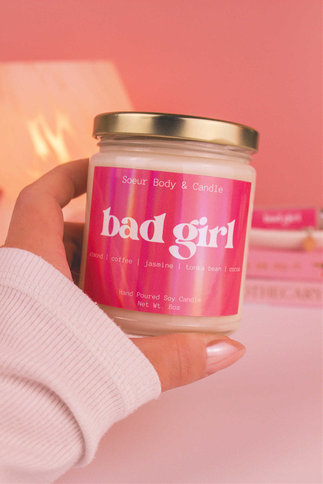 Close-up of a hand holding Bad Girl candle, emphasizing its bold almond, coffee, jasmine, tonka bean, and cocoa aroma.