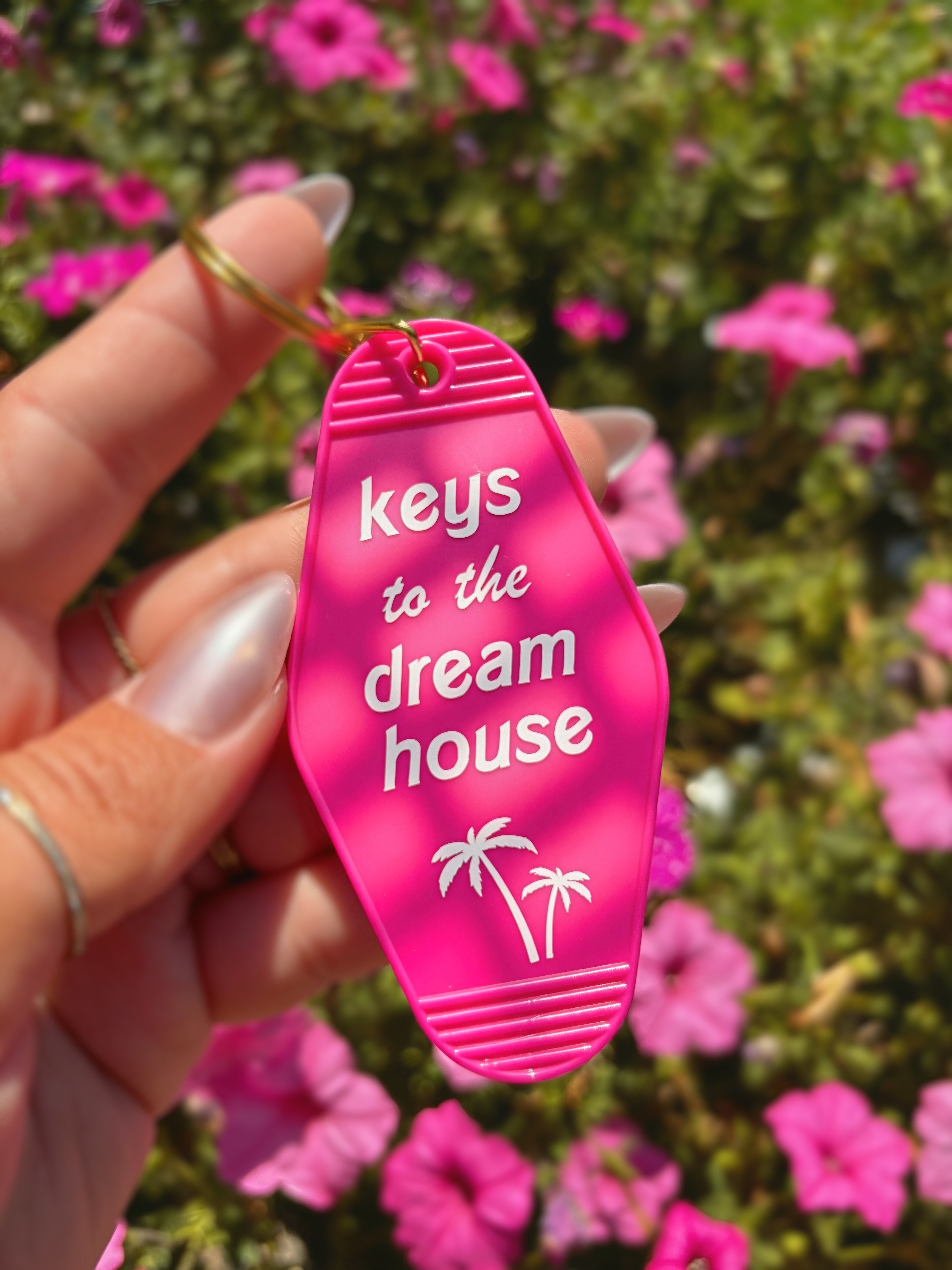 A hand holds a bright pink retro motel-style keychain tag with the phrase &