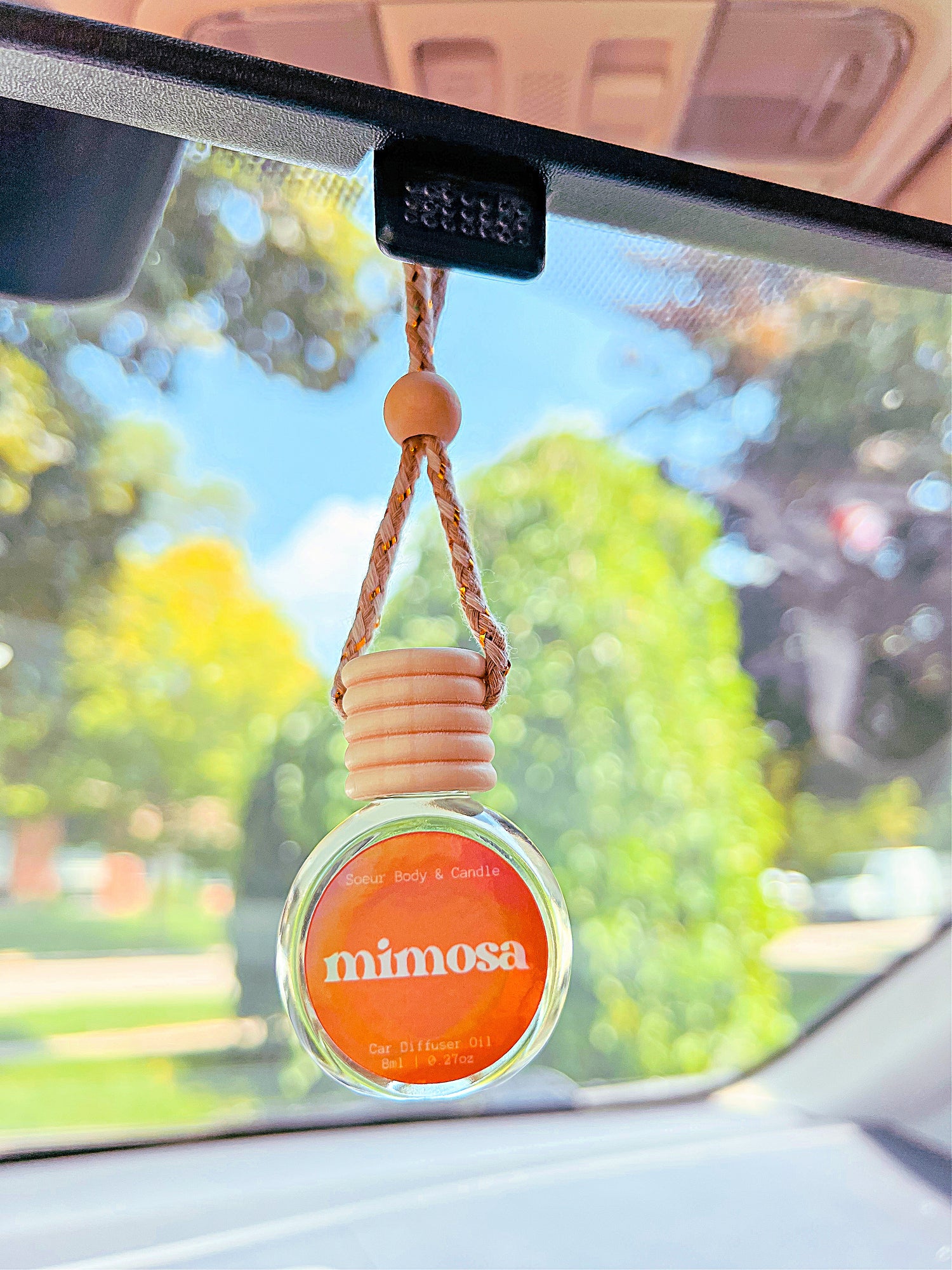 Mimosa Diffuser Oil hanging from a rearview mirror, offering a balanced, long-lasting fragrance of orange, neroli, honeysuckle, and vanilla. Perfect for cars, closets, lockers, and more.