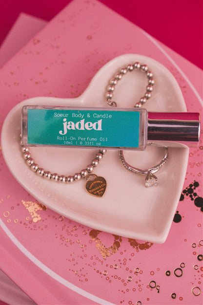 Jaded roll-on perfume bottle displayed in a jewelry dish beside a ring and bracelet, highlighting its deep, earthy notes of spruce, pine, amber, vetiver, and musk.