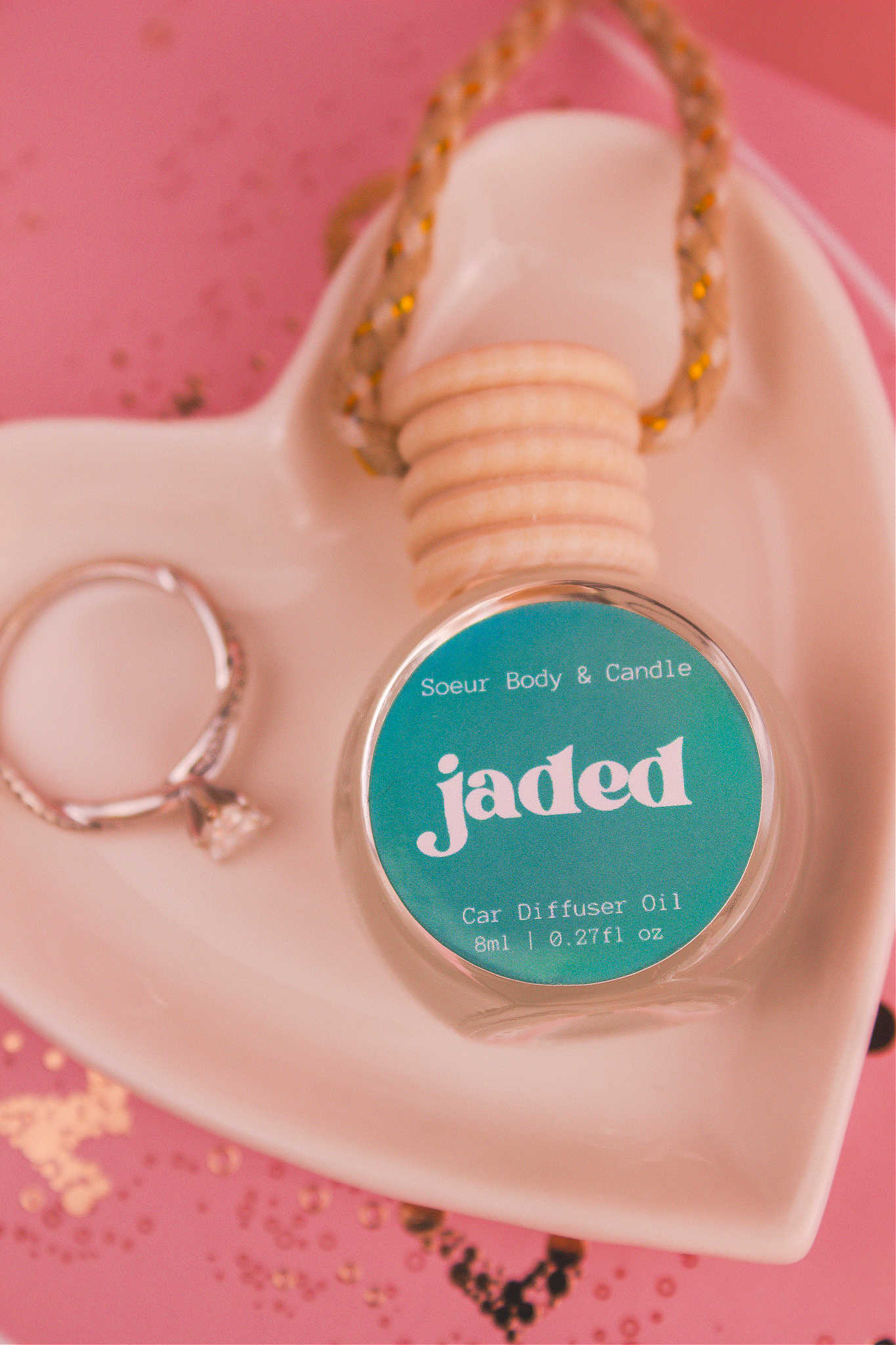 Close-up of Jaded car diffuser in a jewelry dish with a ring beside it, featuring a complex blend of spruce, pine, amber, vetiver, and musk.